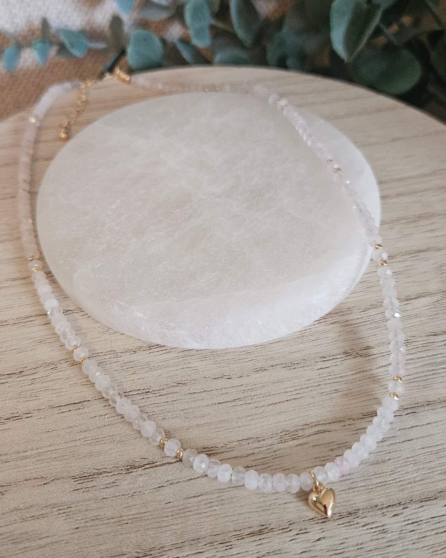 Full Rose Quartz heart necklace arranged around a round selenite plate on a light wooden surface