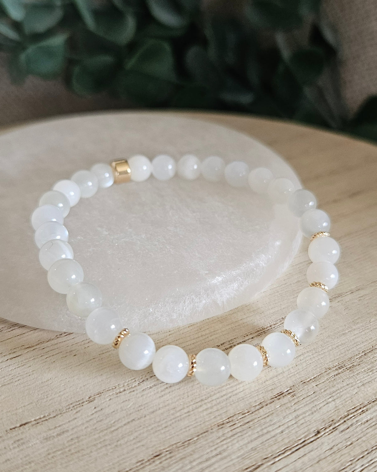 White Moonstone Grace bracelet with 6mm white gemstone beads and gold-plated accents styled on selenite with greenery behind it