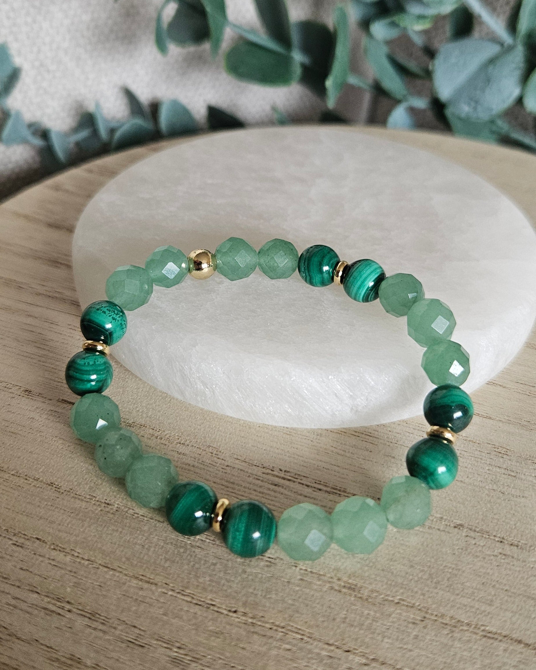 Green Aventurine and Malachite bracelet displayed on light wood beside a round selenite plate