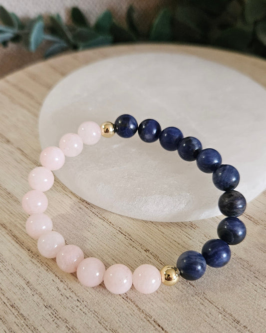 Half-and-half Peach Jade and Sodalite stretch bracelet with gold-plated accents displayed beside a round selenite plate