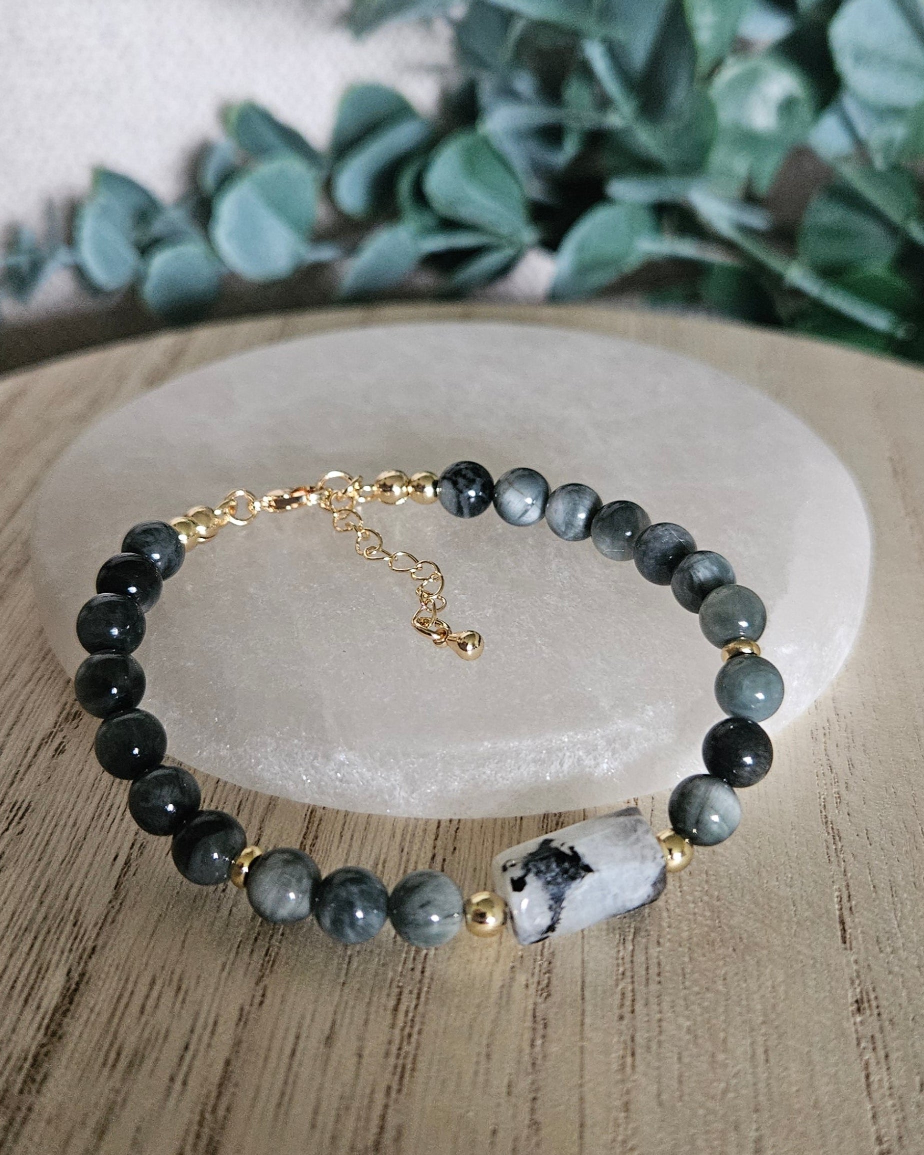 Hawk’s Eye and Moonstone bracelet arranged before a round selenite plate with eucalyptus in the background
