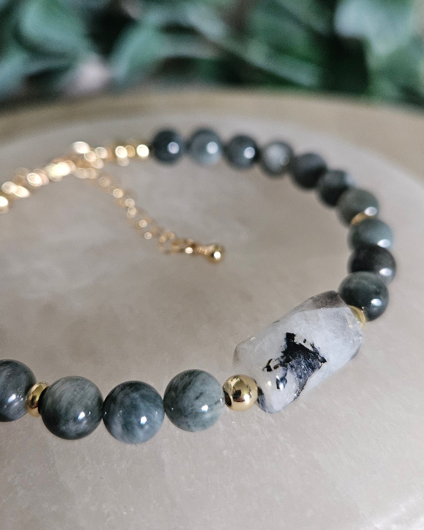 Detailed view of the black Tourmaline inclusions within the Moonstone focal beside Hawk’s Eye beads