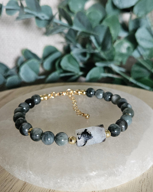 Hawk’s Eye bracelet with a Moonstone focal containing black Tourmaline inclusions displayed on a round selenite plate