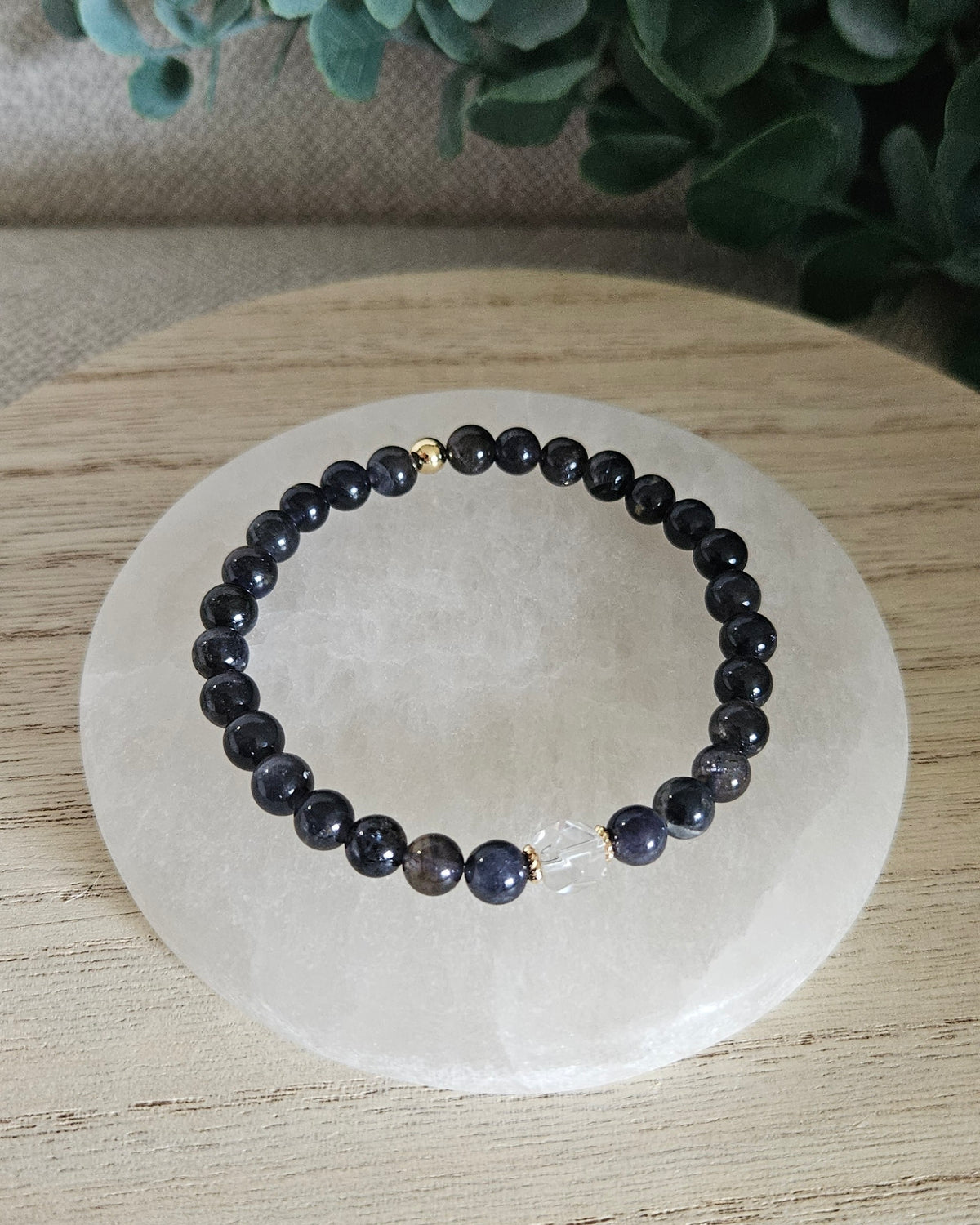 Iolite Still bracelet with dark blue 6mm gemstone beads and Clear Quartz hexagon focal styled on selenite with greenery in the background