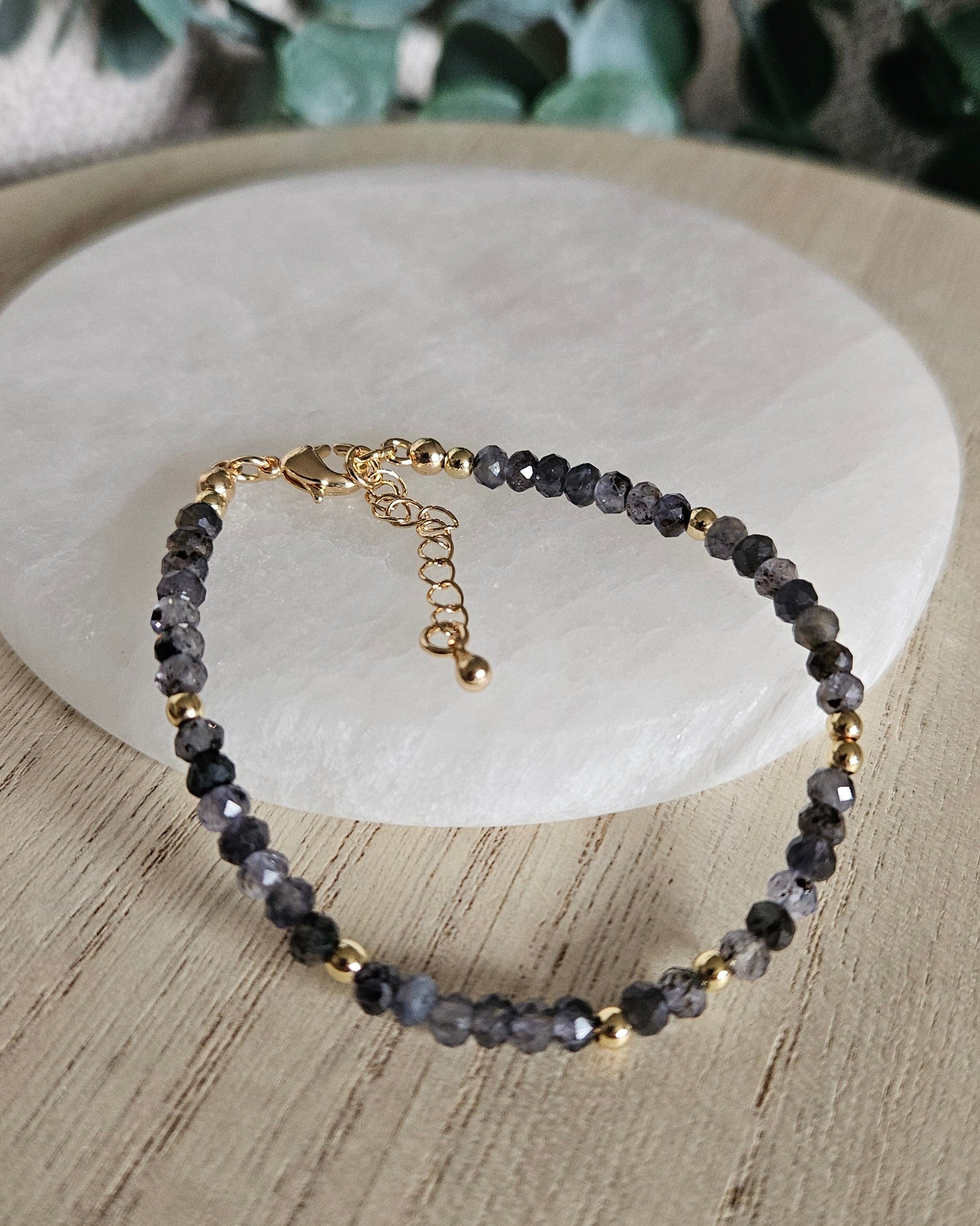 Iolite rondelle bracelet arranged before a round selenite plate with eucalyptus in the background