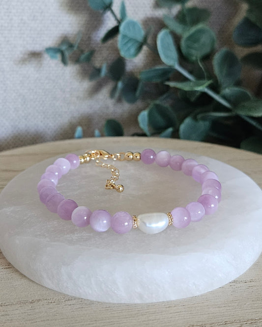 Kunzite Embrace bracelet with 6mm lilac beads, freshwater pearl focal, 14k gold-plated accents and extender chain displayed on selenite