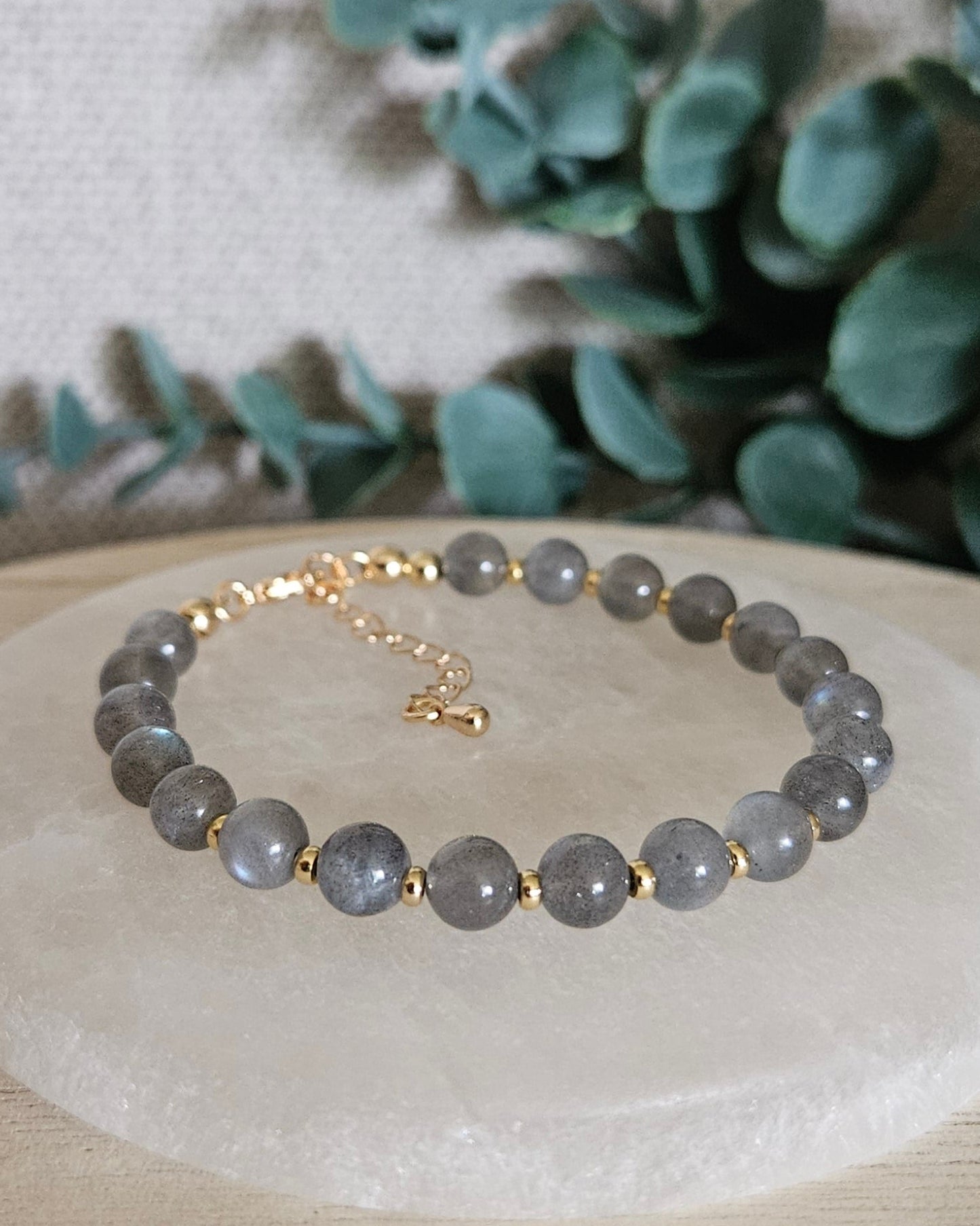 Labradorite Echo bracelet with gold-plated accents and clasp displayed on a round selenite plate