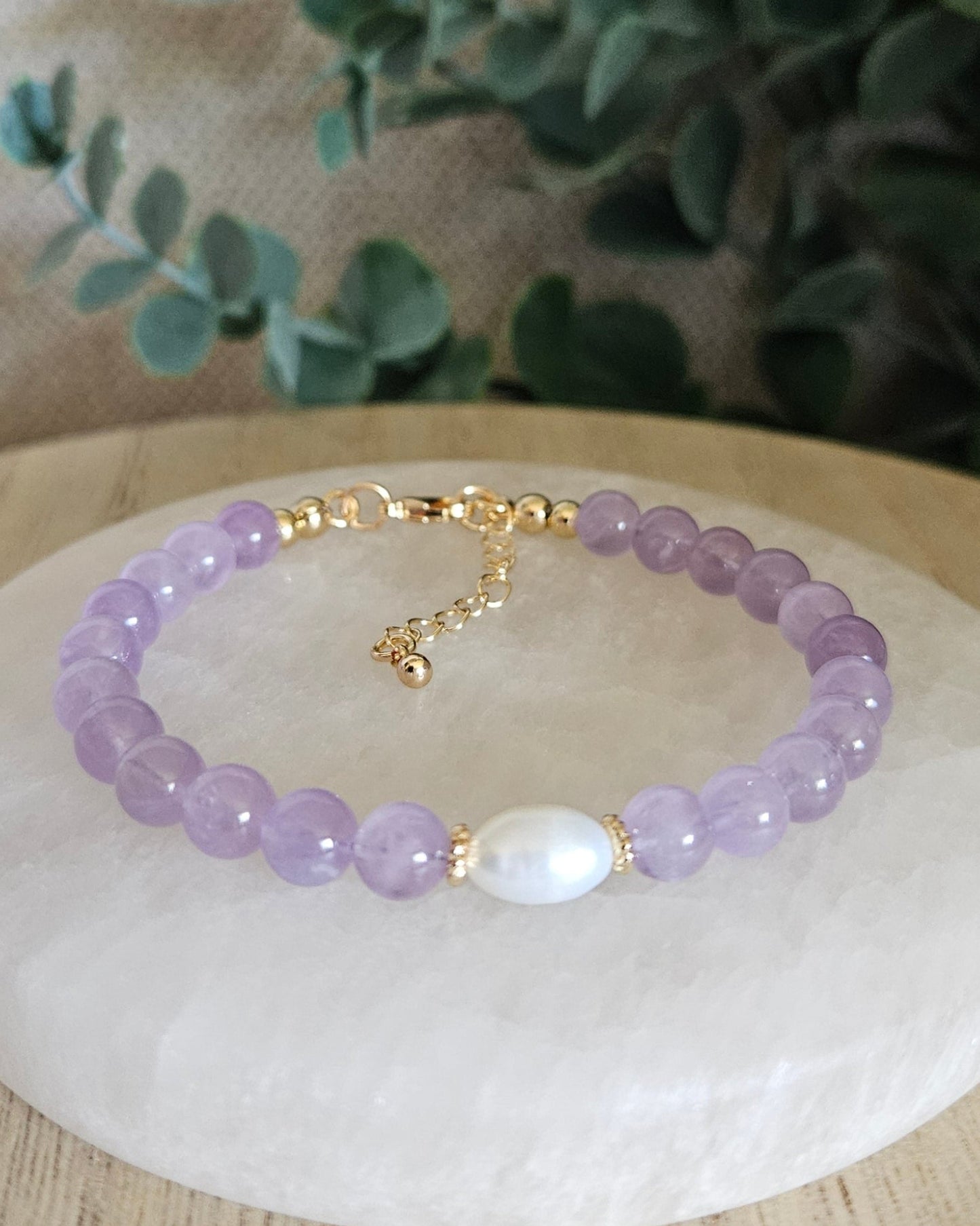 Lavender Amethyst Embrace bracelet with freshwater pearl focal and gold-plated accents displayed on a selenite plate
