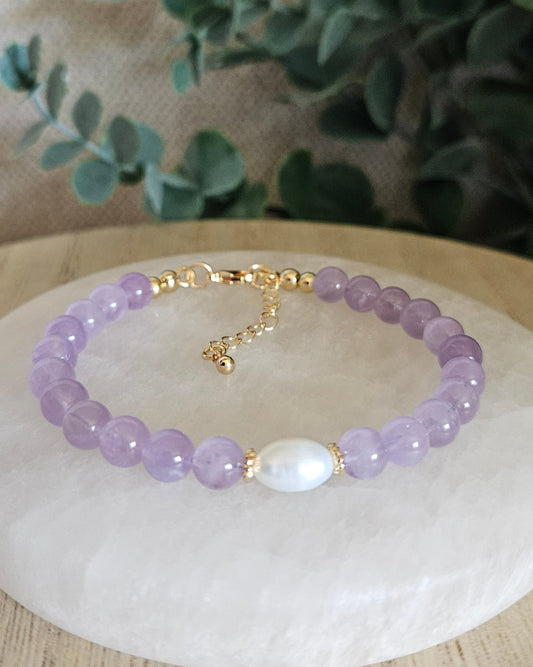 Lavender Amethyst Embrace bracelet with freshwater pearl focal and gold-plated accents displayed on a selenite plate
