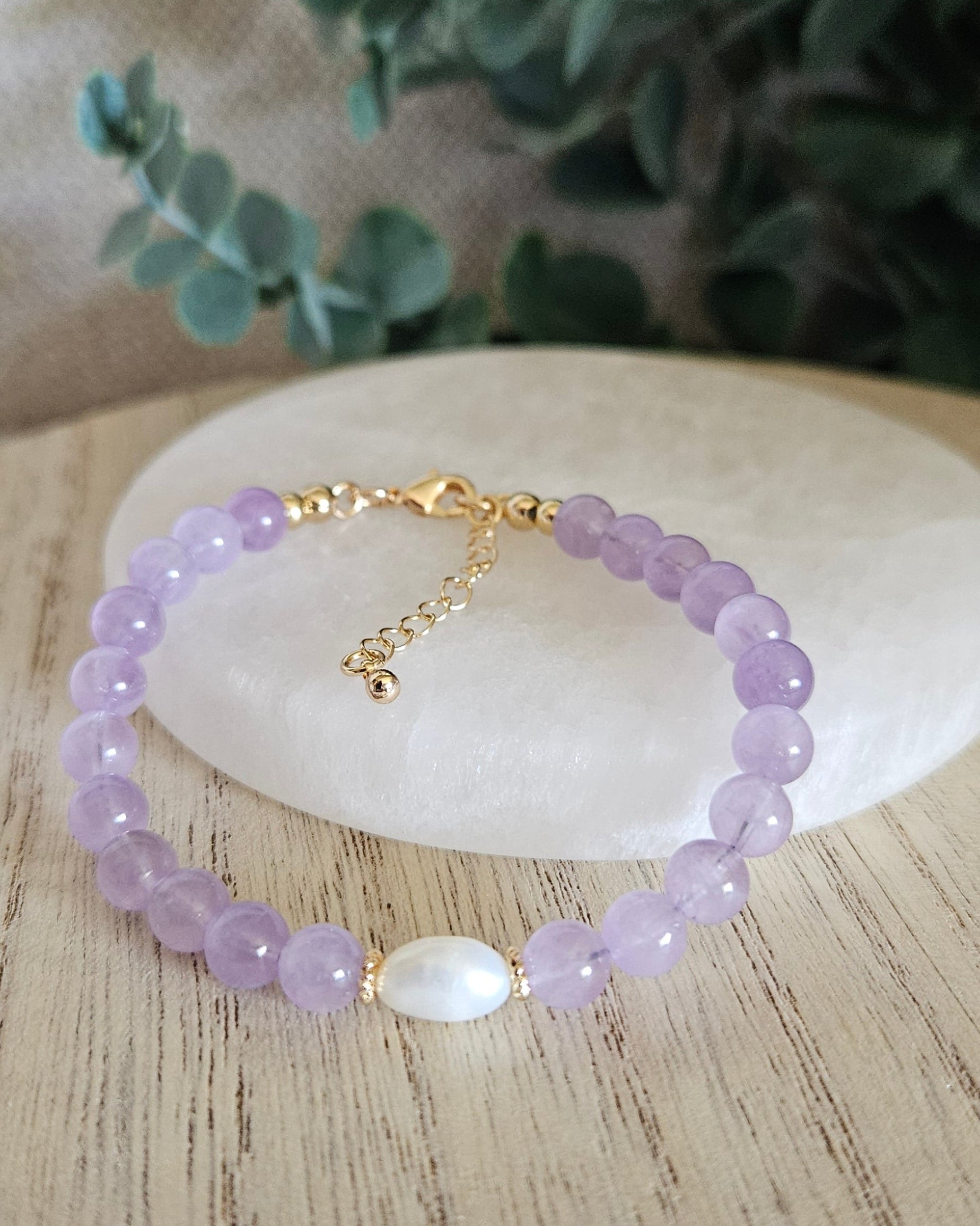 Lavender Amethyst Embrace bracelet arranged before a selenite plate with a freshwater pearl focal and eucalyptus background