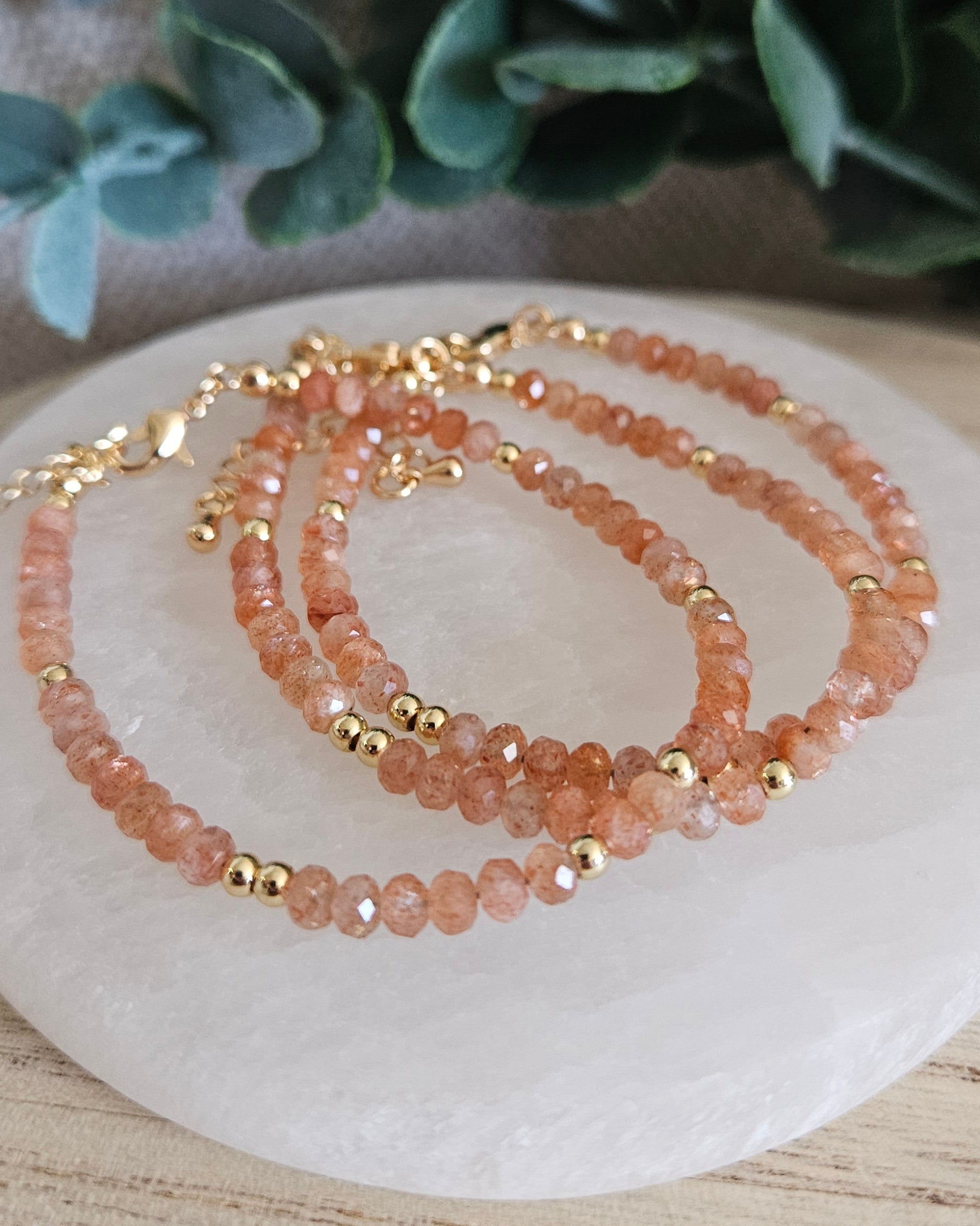 Layered Sunstone rondelle bracelets with gold-plated spacer beads arranged on a round selenite plate