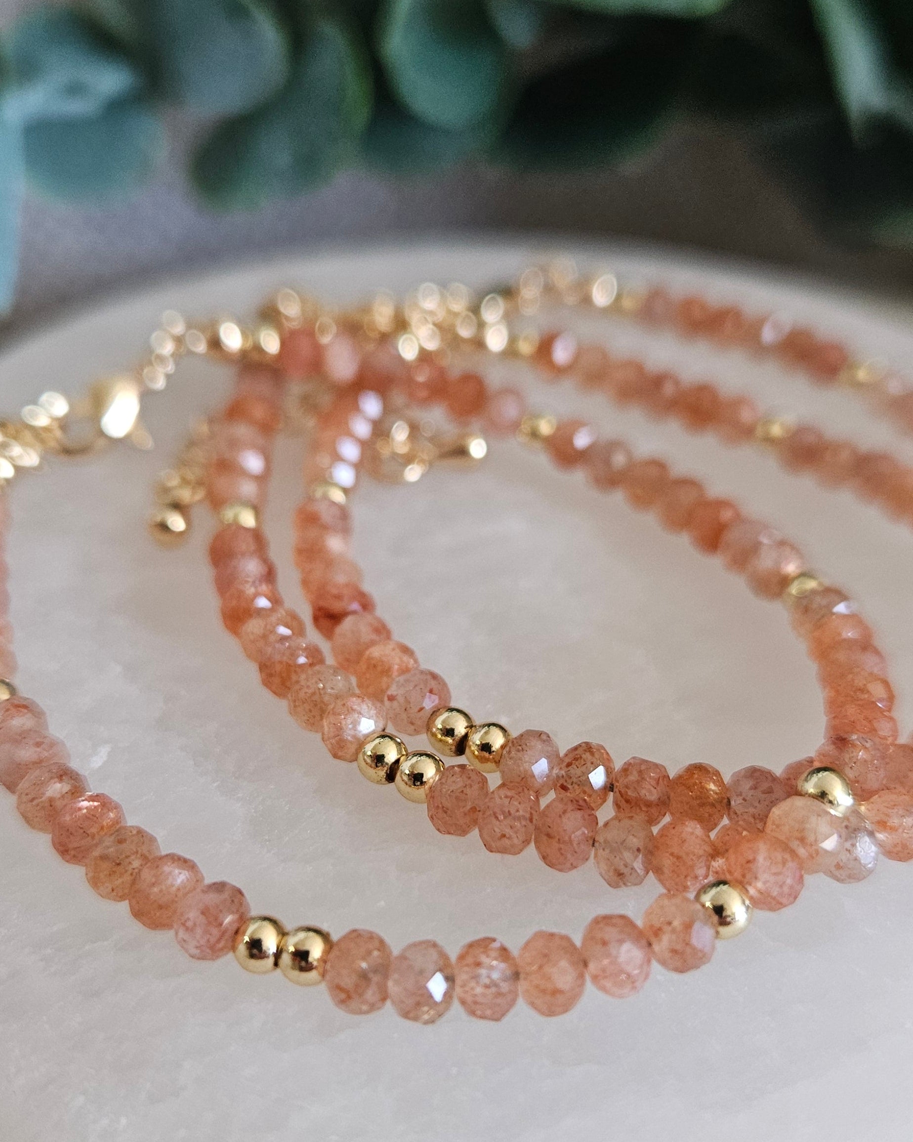 Layered peach Sunstone bracelets with gold-plated accents displayed on selenite with eucalyptus in the background