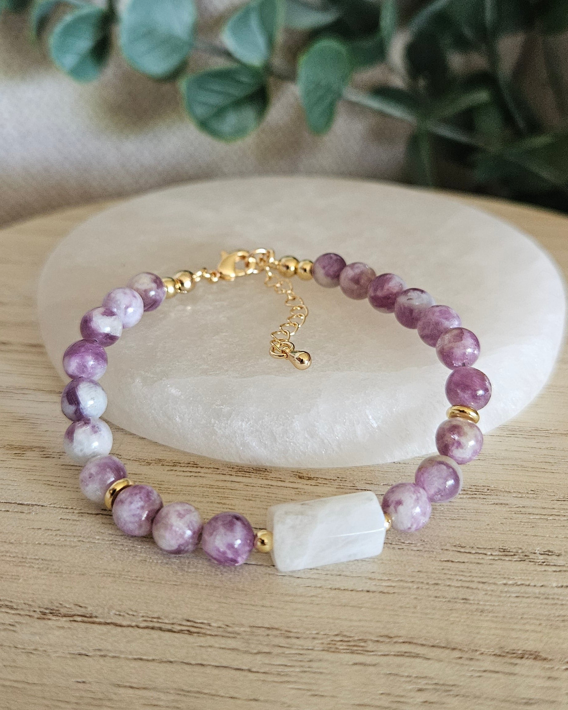 Lepidolite and Moonstone bracelet arranged before a round selenite plate with eucalyptus in the background