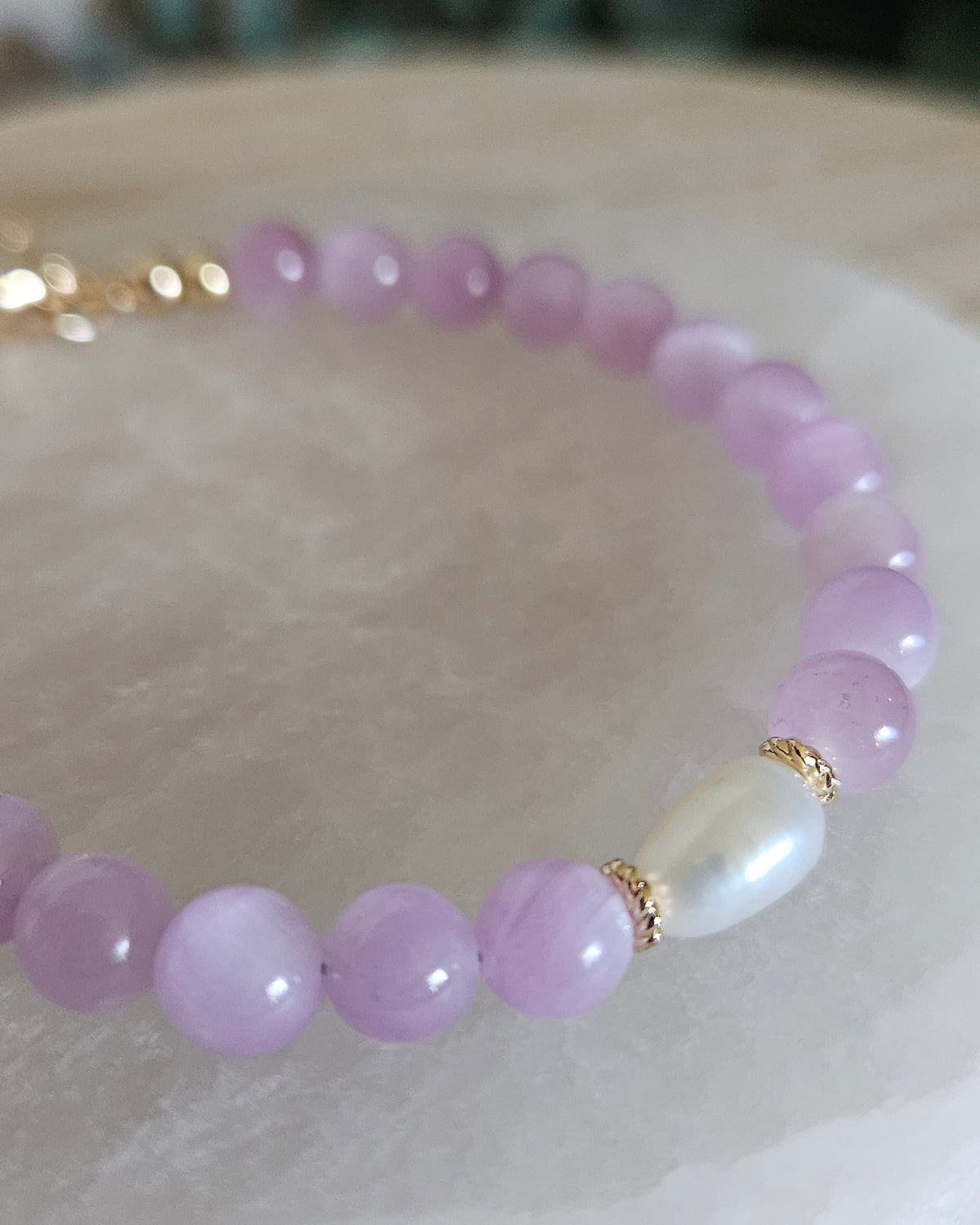 Macro close-up of Kunzite beads, freshwater pearl focal and 14k gold-plated spacer accents displayed on selenite