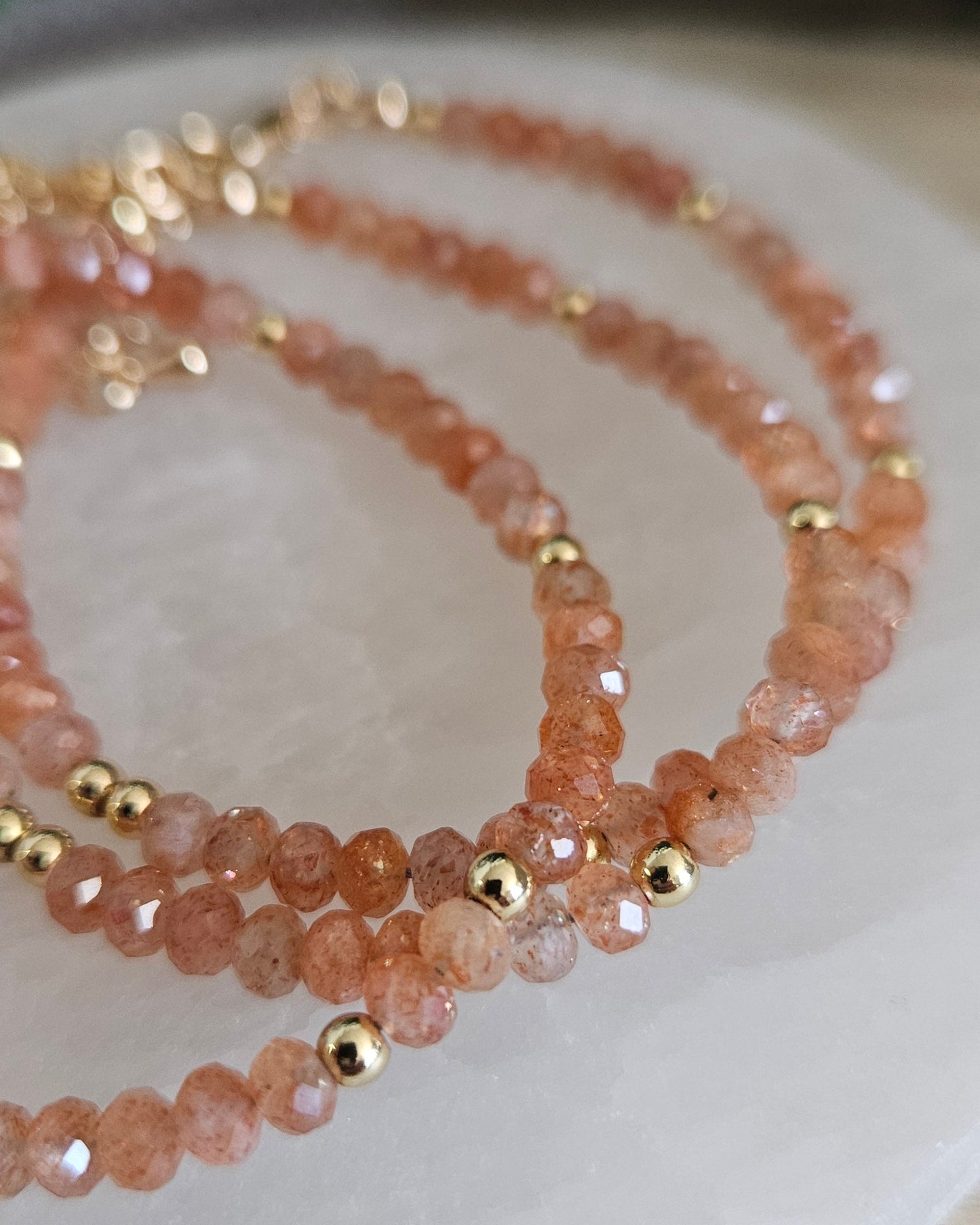 Macro view of layered faceted Sunstone bracelets with polished gold-plated spacer accents
