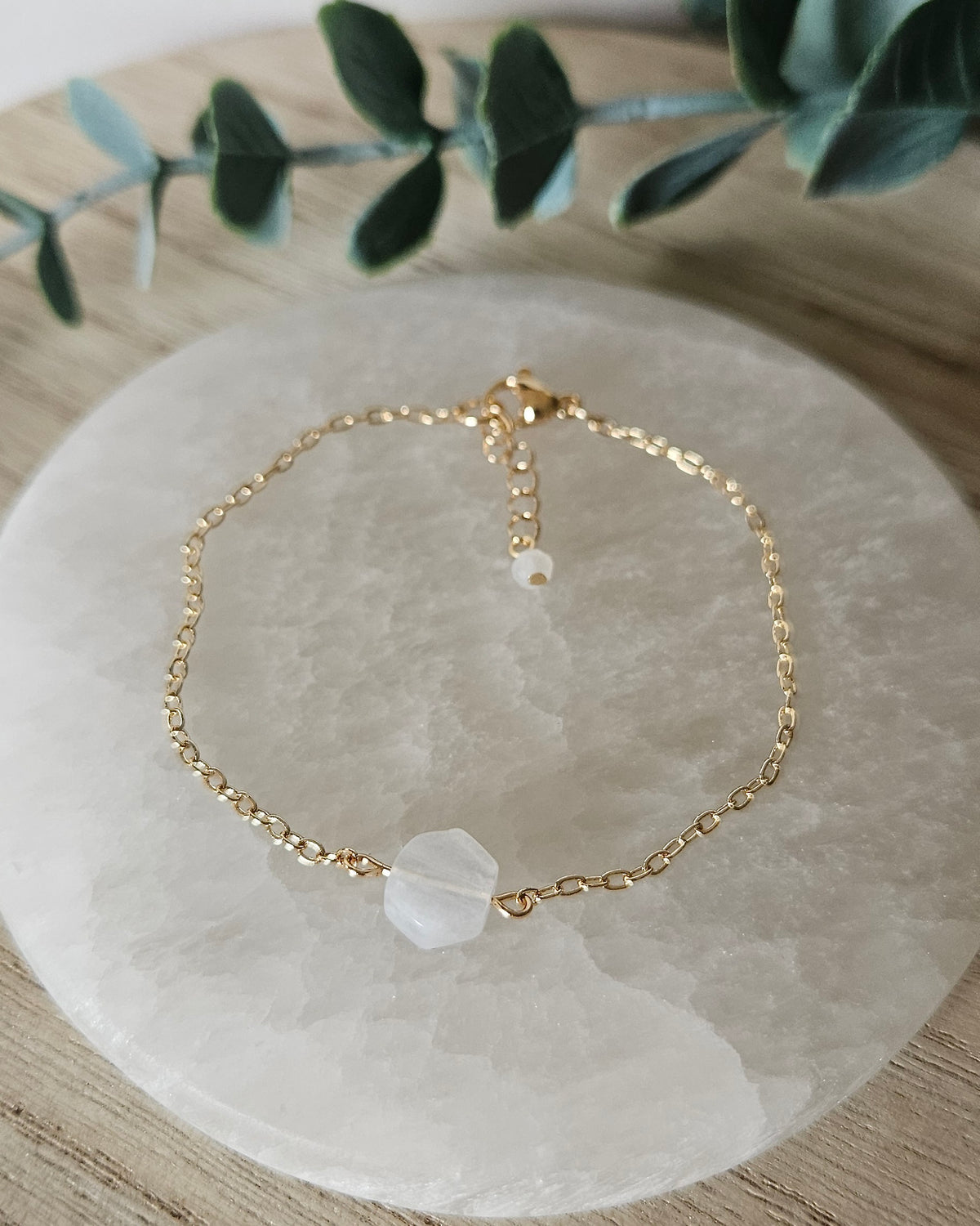 Moonstone Whisper bracelet laid flat on a selenite plate with 14k gold-plated chain, clasp and extender
