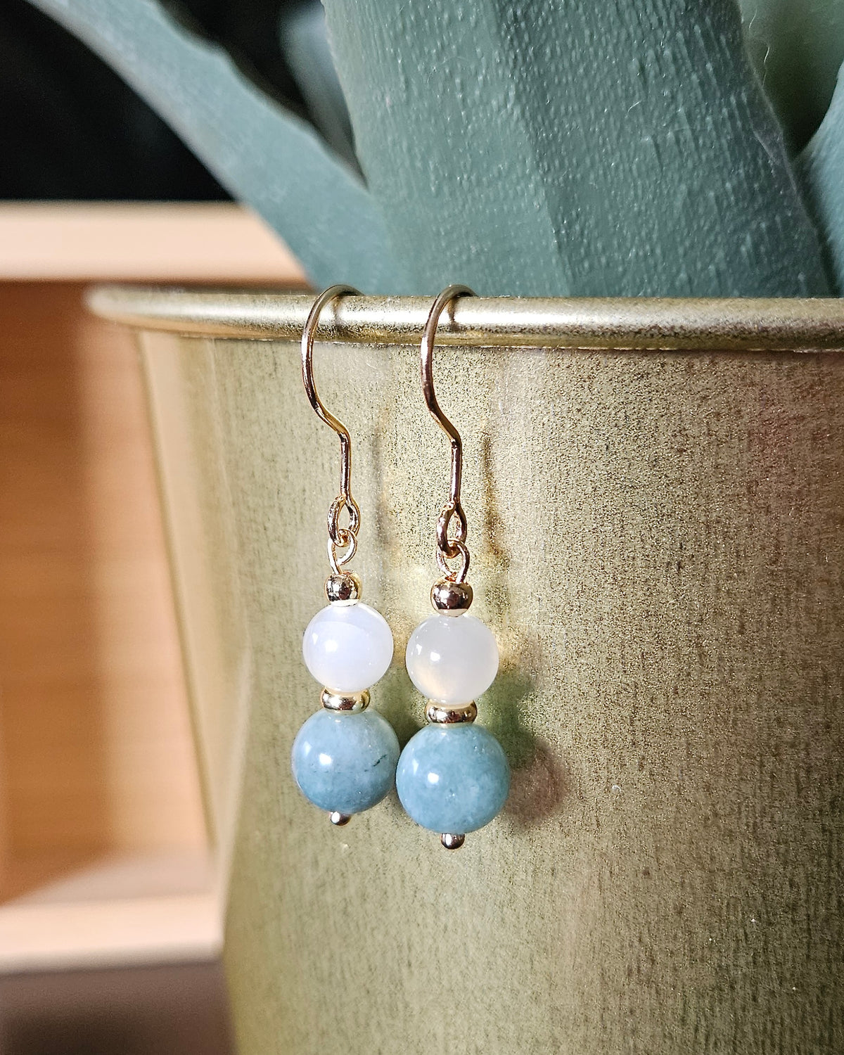 Moonstone and Sage Green Jade earrings hanging in a warm neutral styled setting