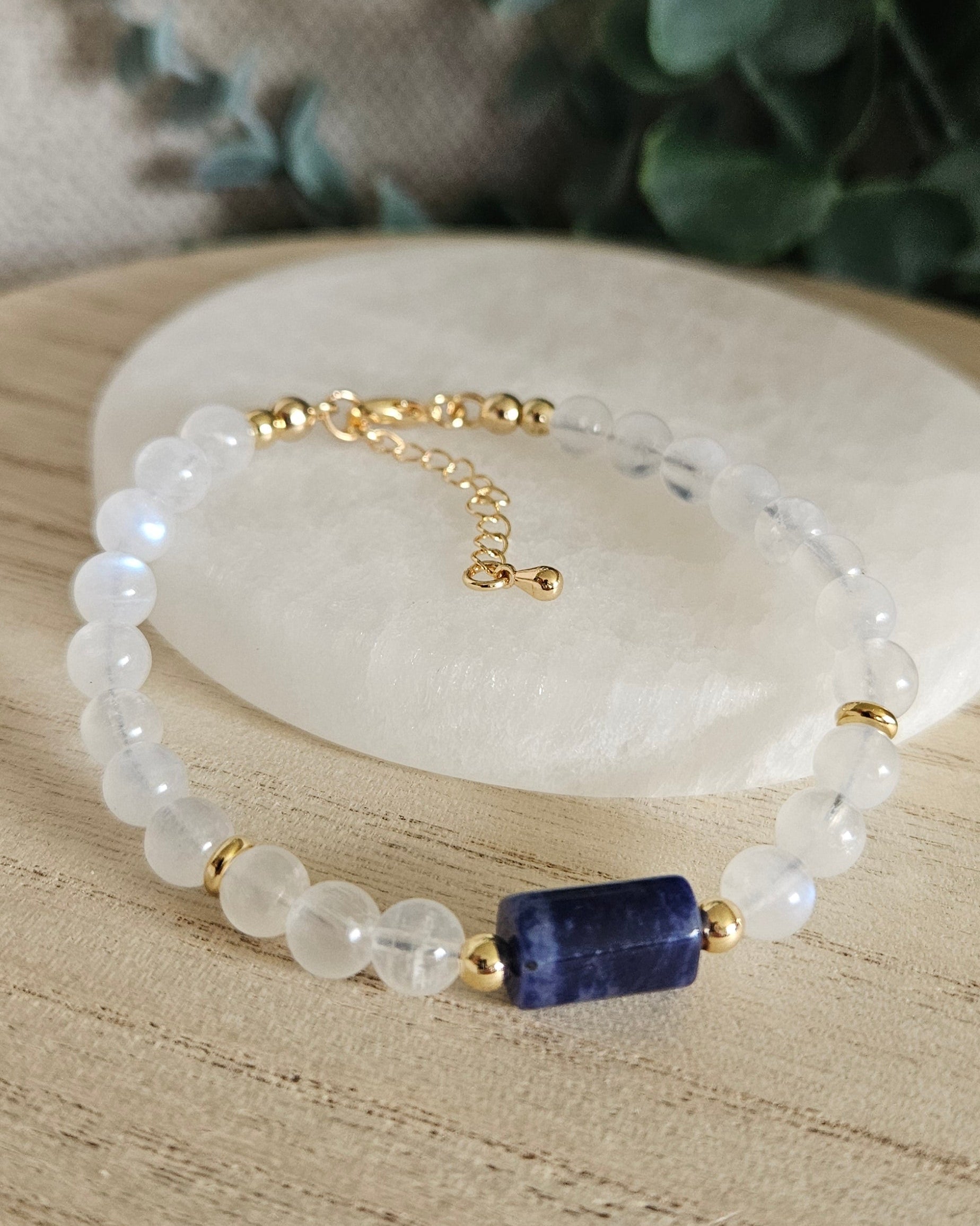 Moonstone and Sodalite bracelet arranged before a round selenite plate with eucalyptus in the background