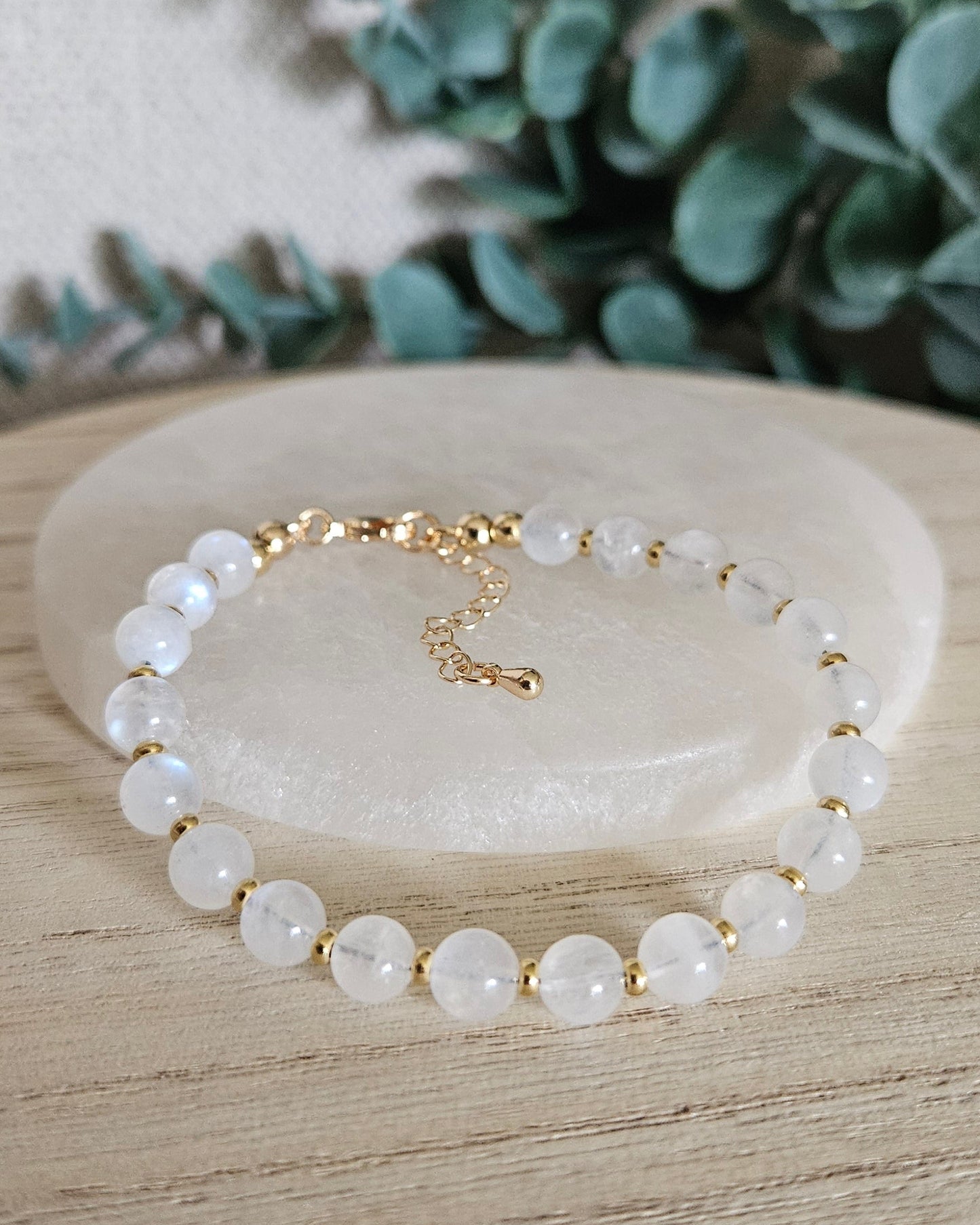 Moonstone Echo bracelet arranged before a selenite plate with eucalyptus in the background