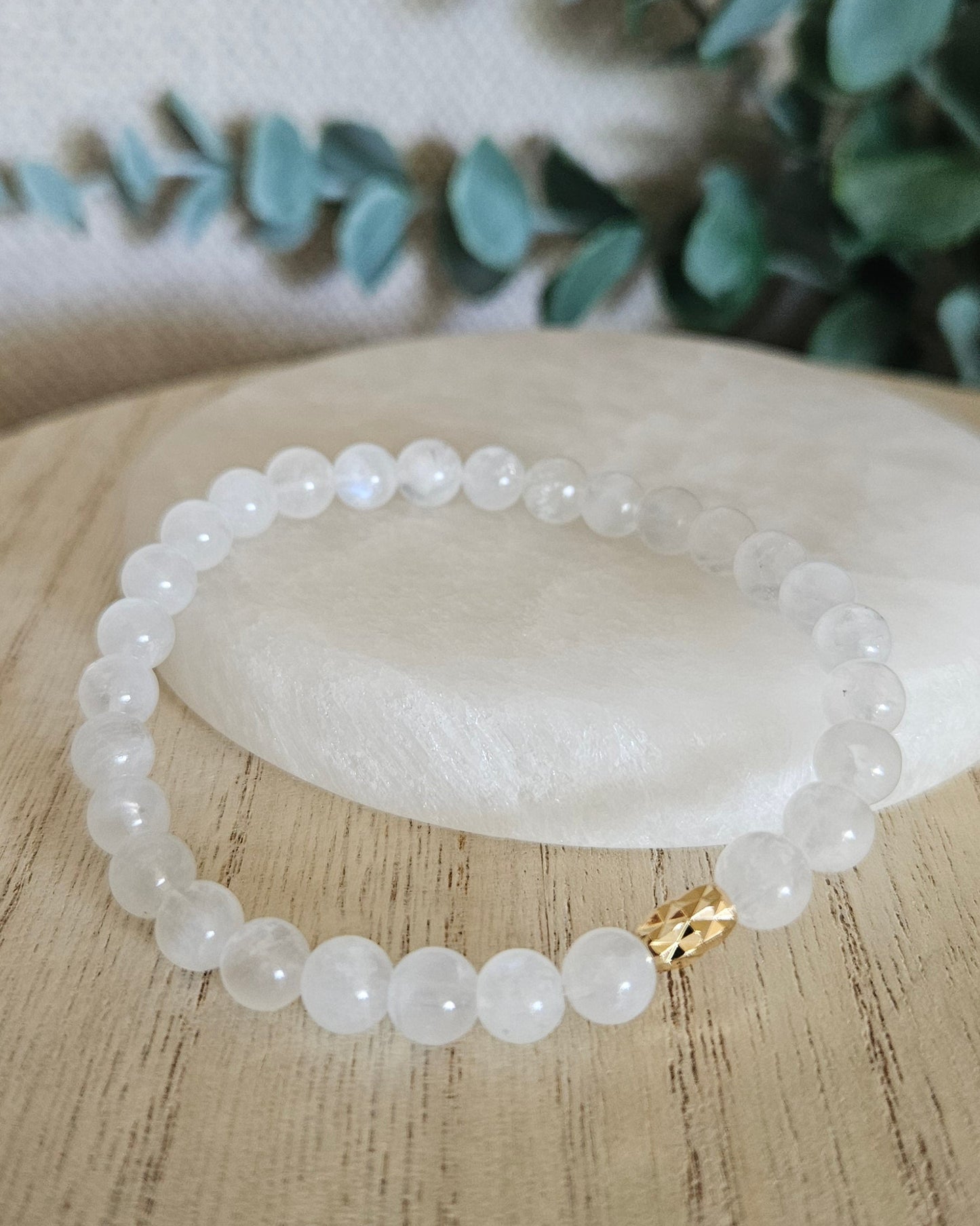 Moonstone bracelet arranged before a round selenite plate with eucalyptus in the background