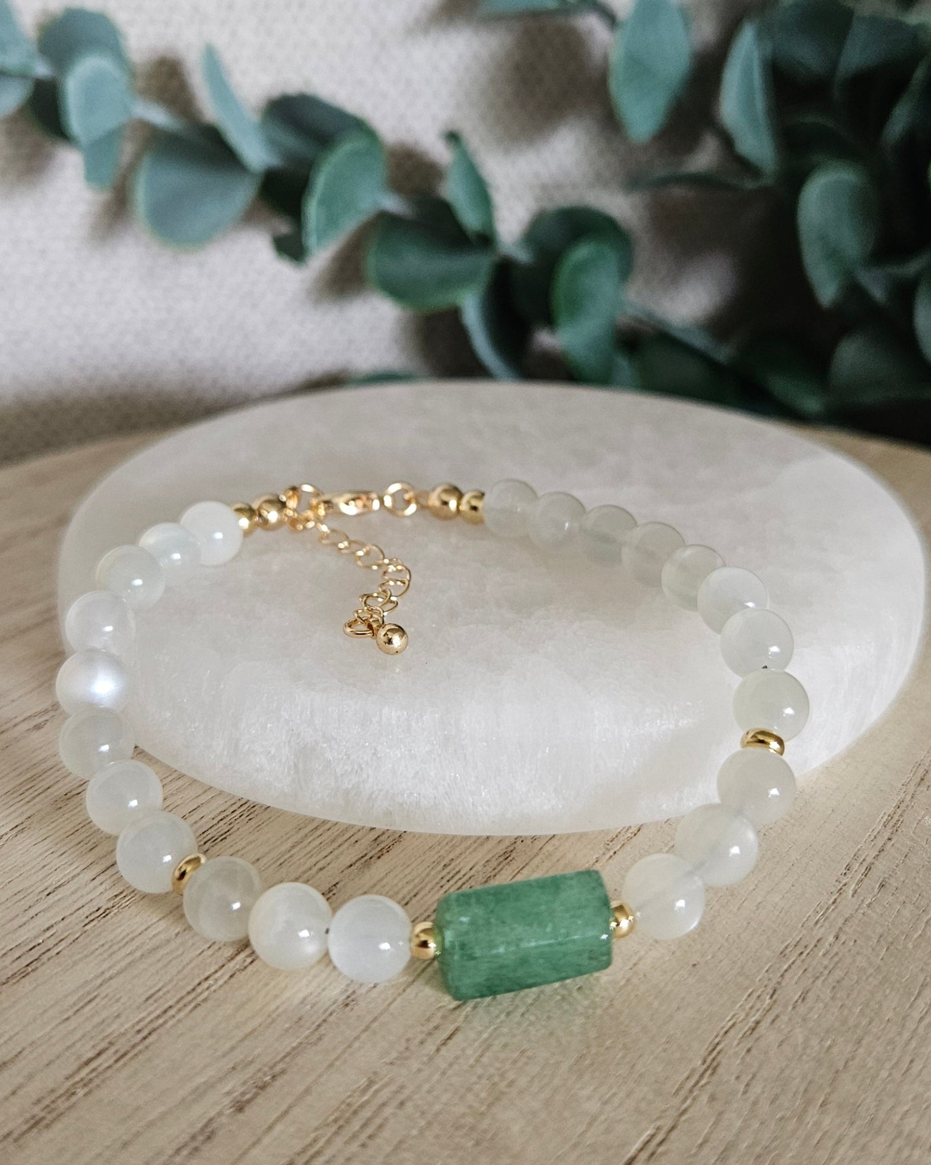 White Moonstone and Green Strawberry Quartz bracelet arranged before a selenite plate with eucalyptus in the background