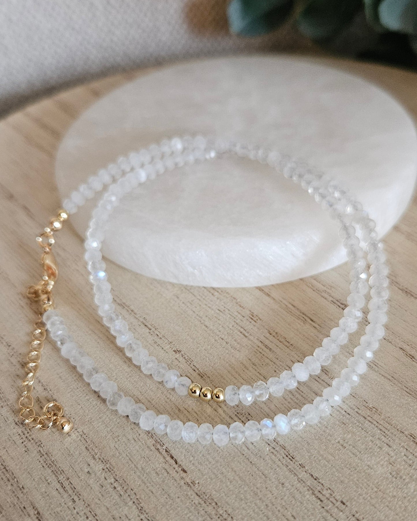 Moonstone necklace with gold-plated clasp and extender chain arranged beside a round selenite plate