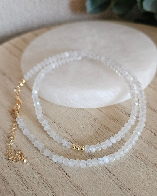 Moonstone necklace with gold-plated clasp and extender chain arranged beside a round selenite plate