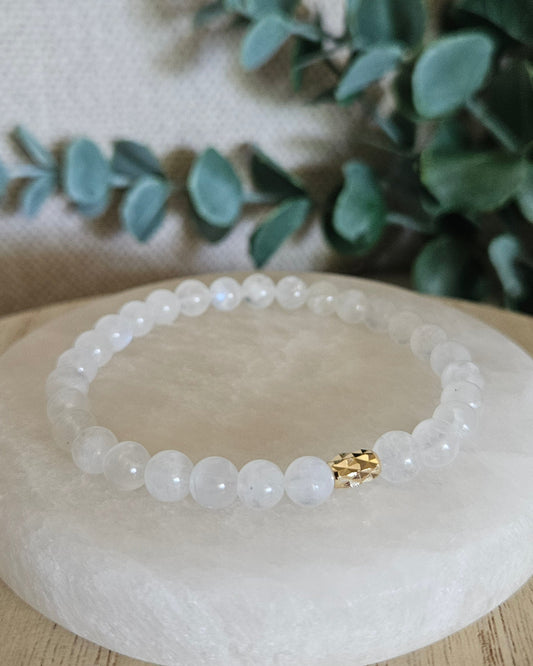 Moonstone stretch bracelet with a diamond-cut gold-filled oval focal displayed on a round selenite plate