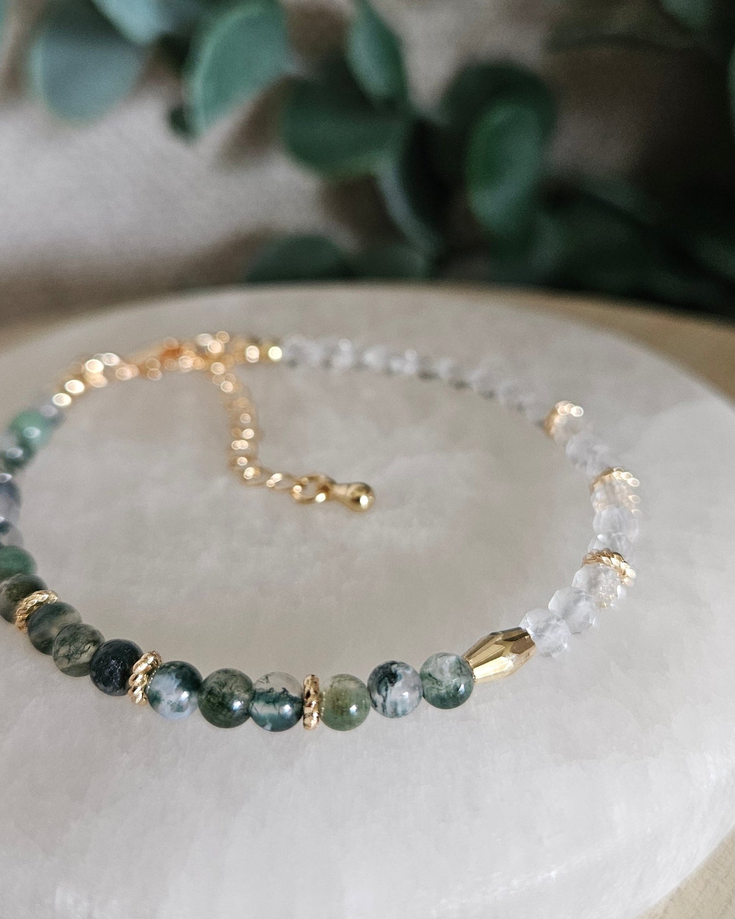 Close-up of round Moss Agate beads, faceted Clear Quartz and gold-filled accent beads on selenite