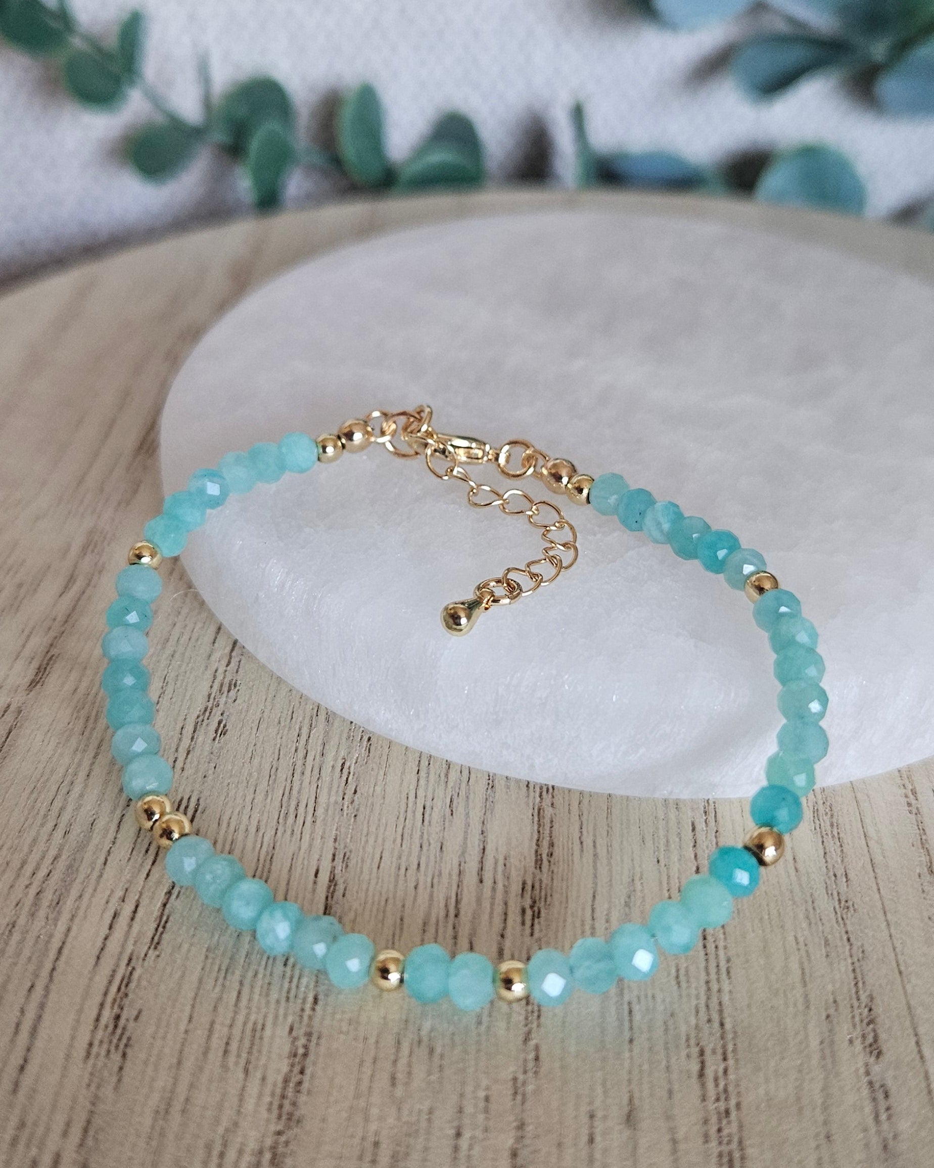 Mozambique Amazonite bracelet displayed on light wood beside a round selenite plate with eucalyptus