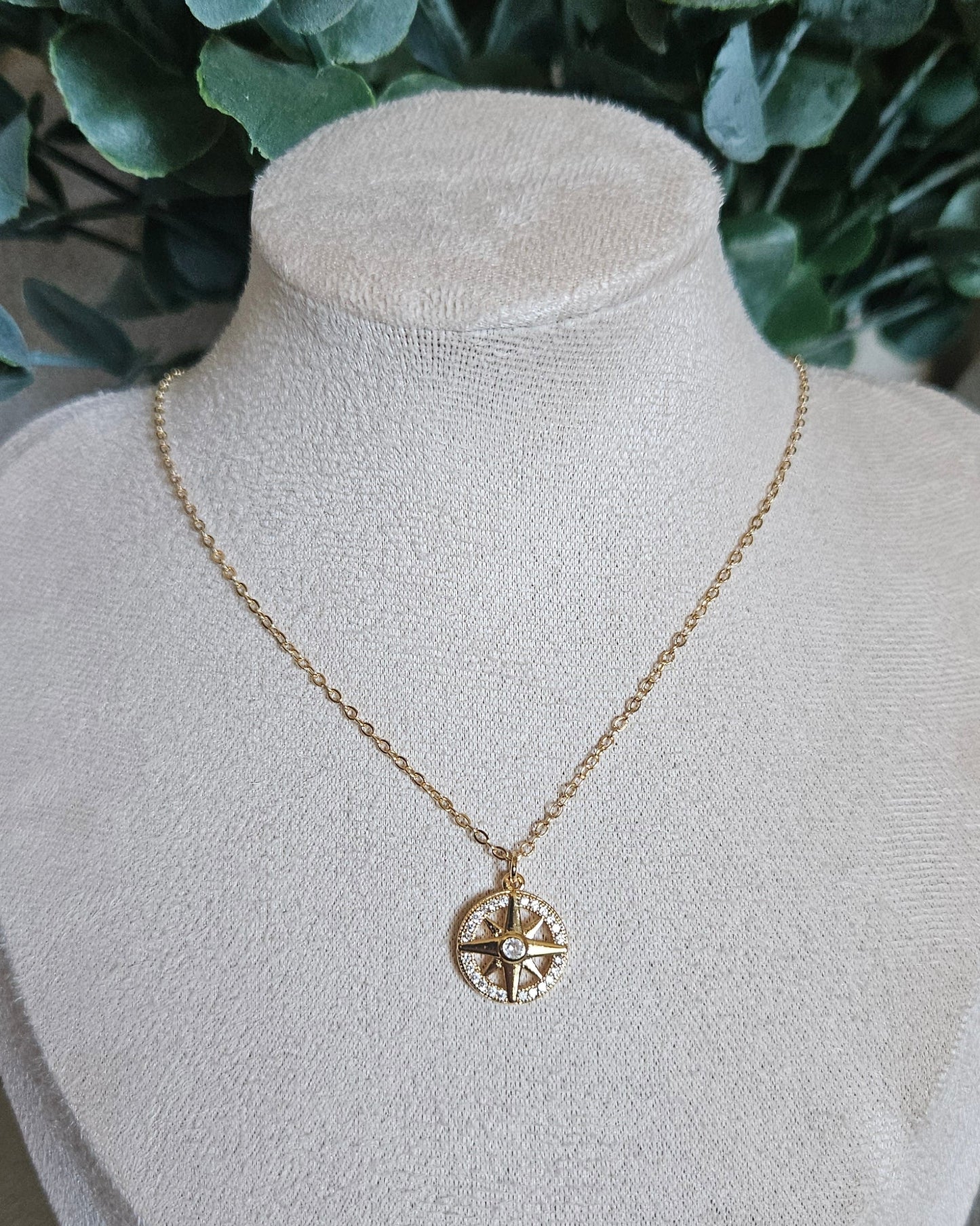 Front view of the 14k gold-filled North Star necklace displayed on a beige jewellery bust with greenery