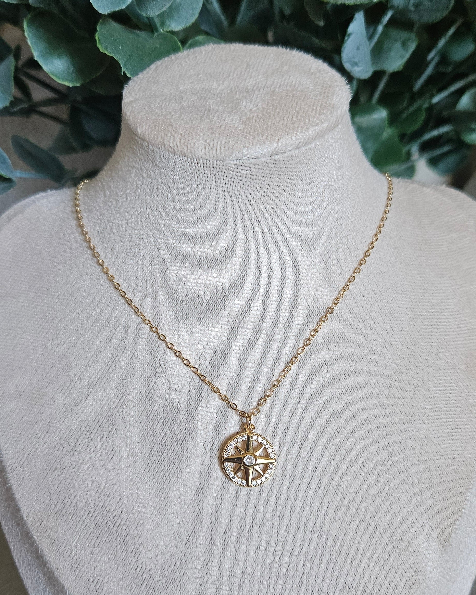 Front view of the 14k gold-filled North Star necklace displayed on a beige jewellery bust with greenery