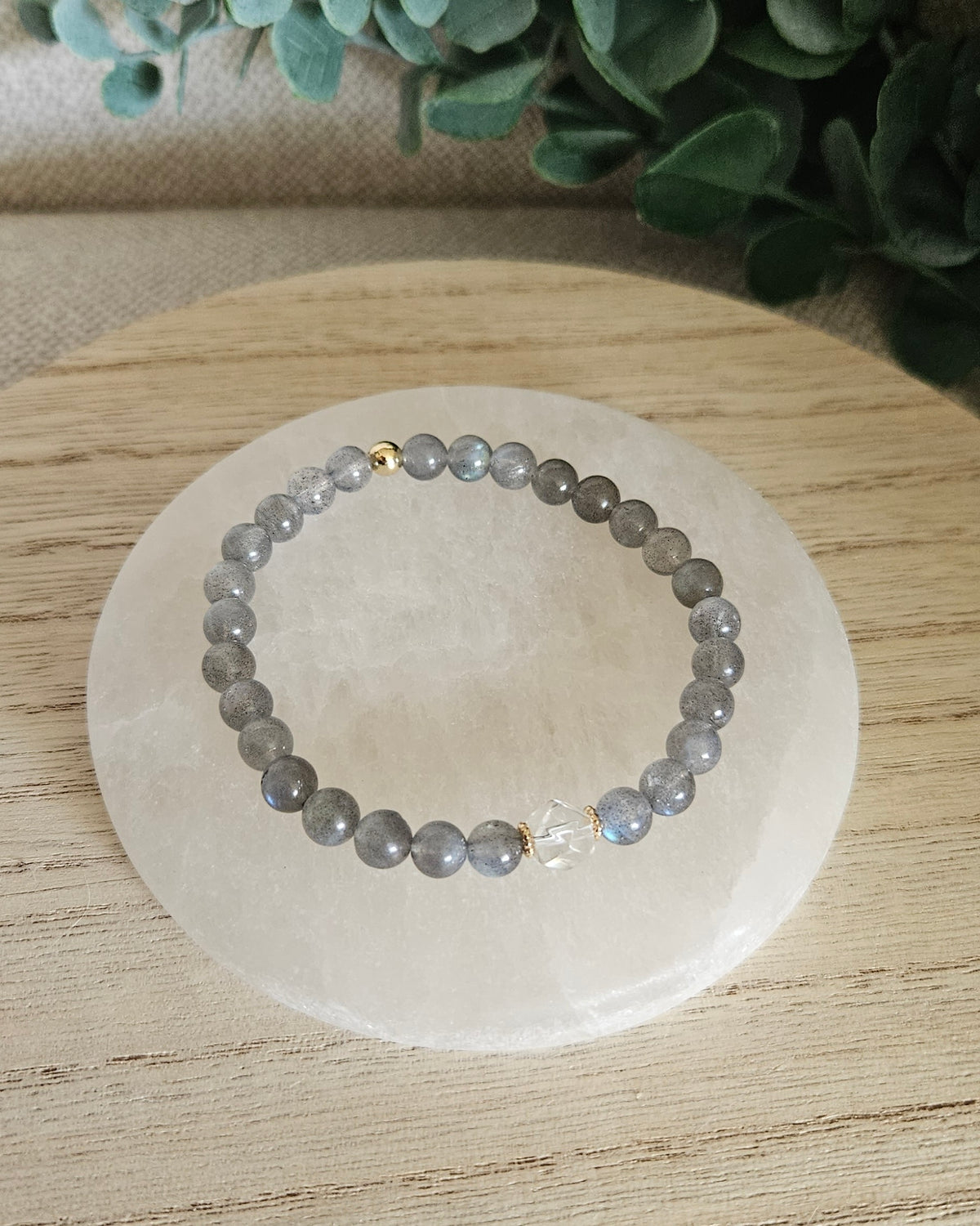 Overhead view of the Labradorite Still bracelet with grey 6mm beads, Clear Quartz focal and gold accent bead on a white selenite plate

