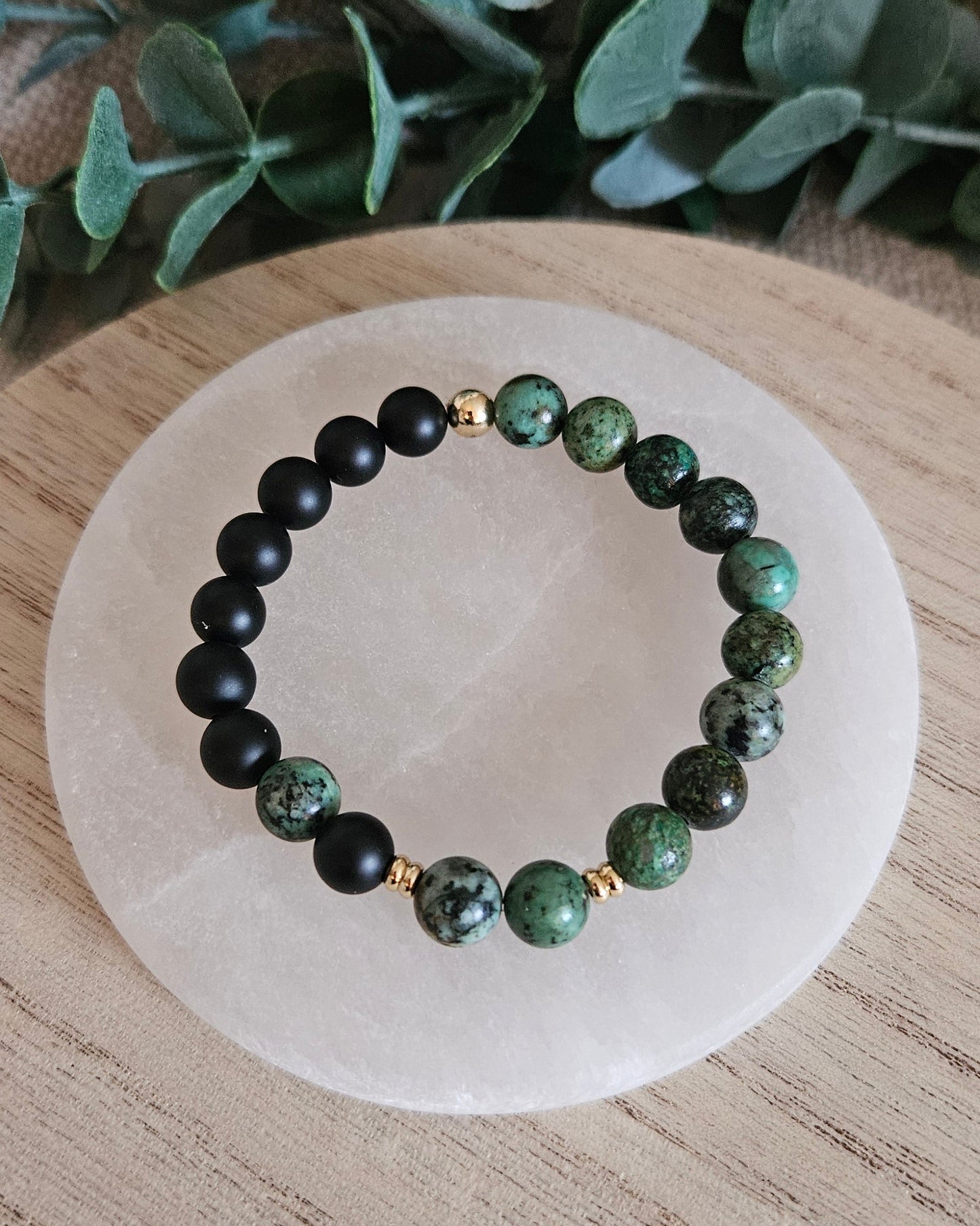 Overhead view of the African Turquoise and Black Onyx bracelet arranged on a round selenite plate