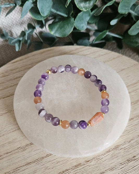 Overhead view of the Amethyst and Sunstone stretch bracelet with gold-plated spacers on a round selenite plate