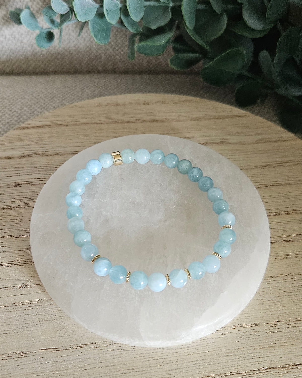 Overhead view of the Aquamarine Grace bracelet with soft blue beads and gold-plated focal accent on a white selenite plate