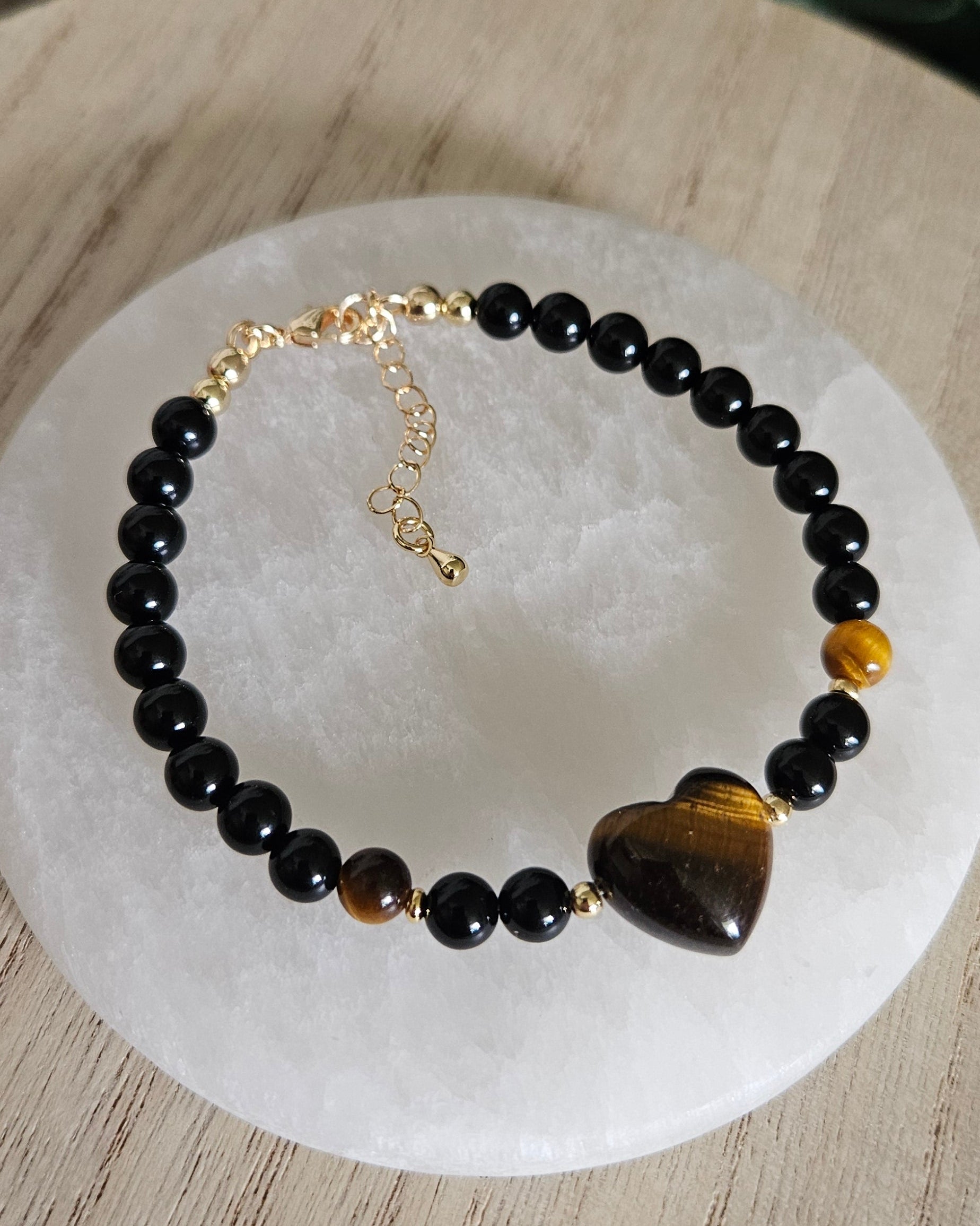 Overhead view of the Black Onyx bracelet with Tiger's Eye heart focal, accent beads and gold extender chain on selenite