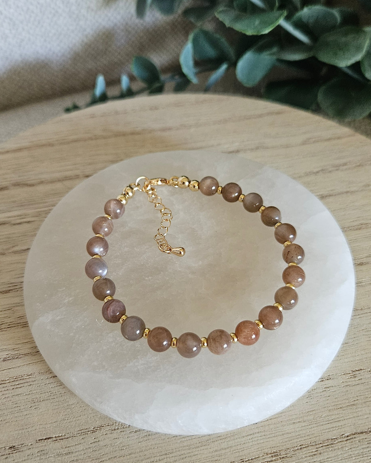 Overhead view of the Chocolate Moonstone Echo bracelet with peach, brown and cream beads, gold-plated accents and extender chain on selenite