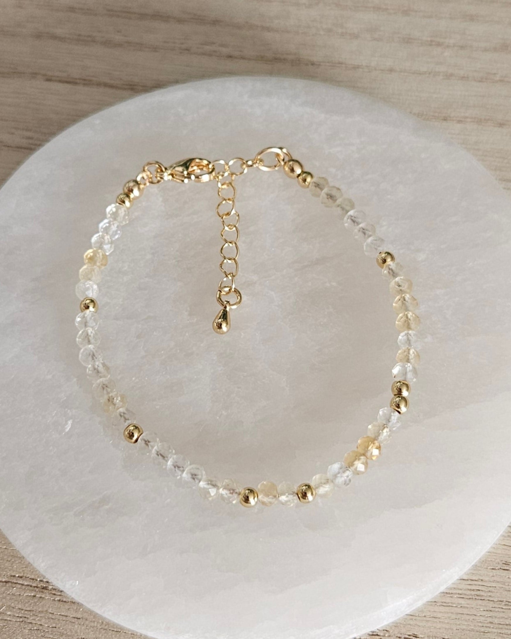 Overhead view of the Citrine bracelet with gold-plated spacer beads, clasp and extender chain on selenite