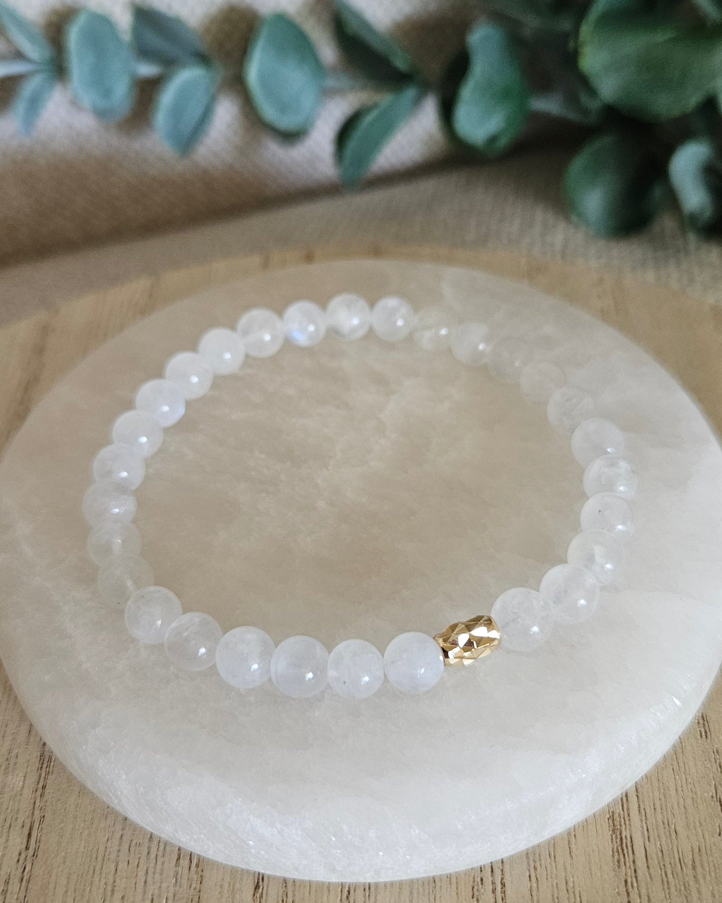 Overhead view of the Moonstone bead bracelet and faceted gold-filled oval focal on a round selenite plate