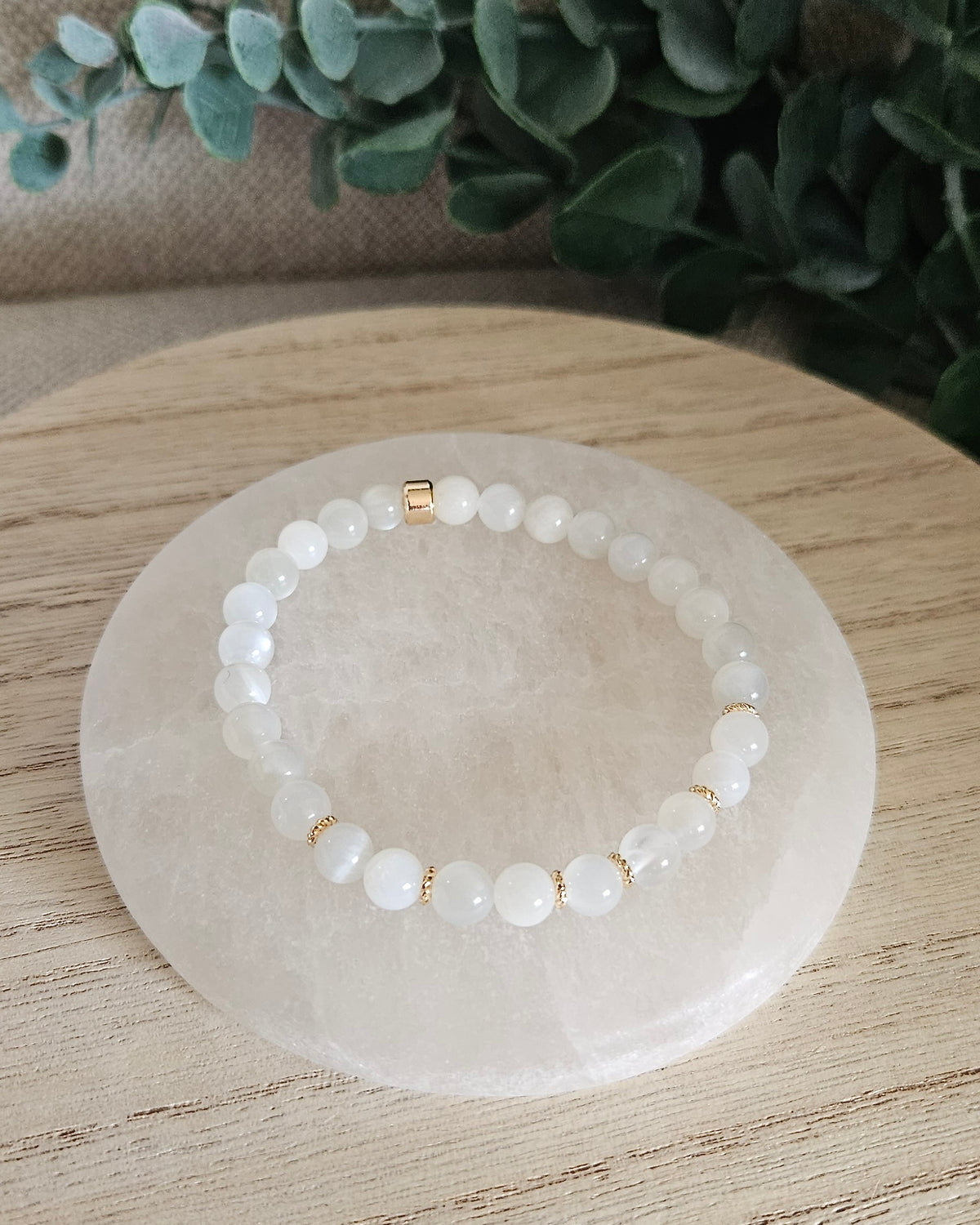 Overhead view of the White Moonstone Grace bracelet with soft white beads and gold-plated focal accent on a white selenite plate