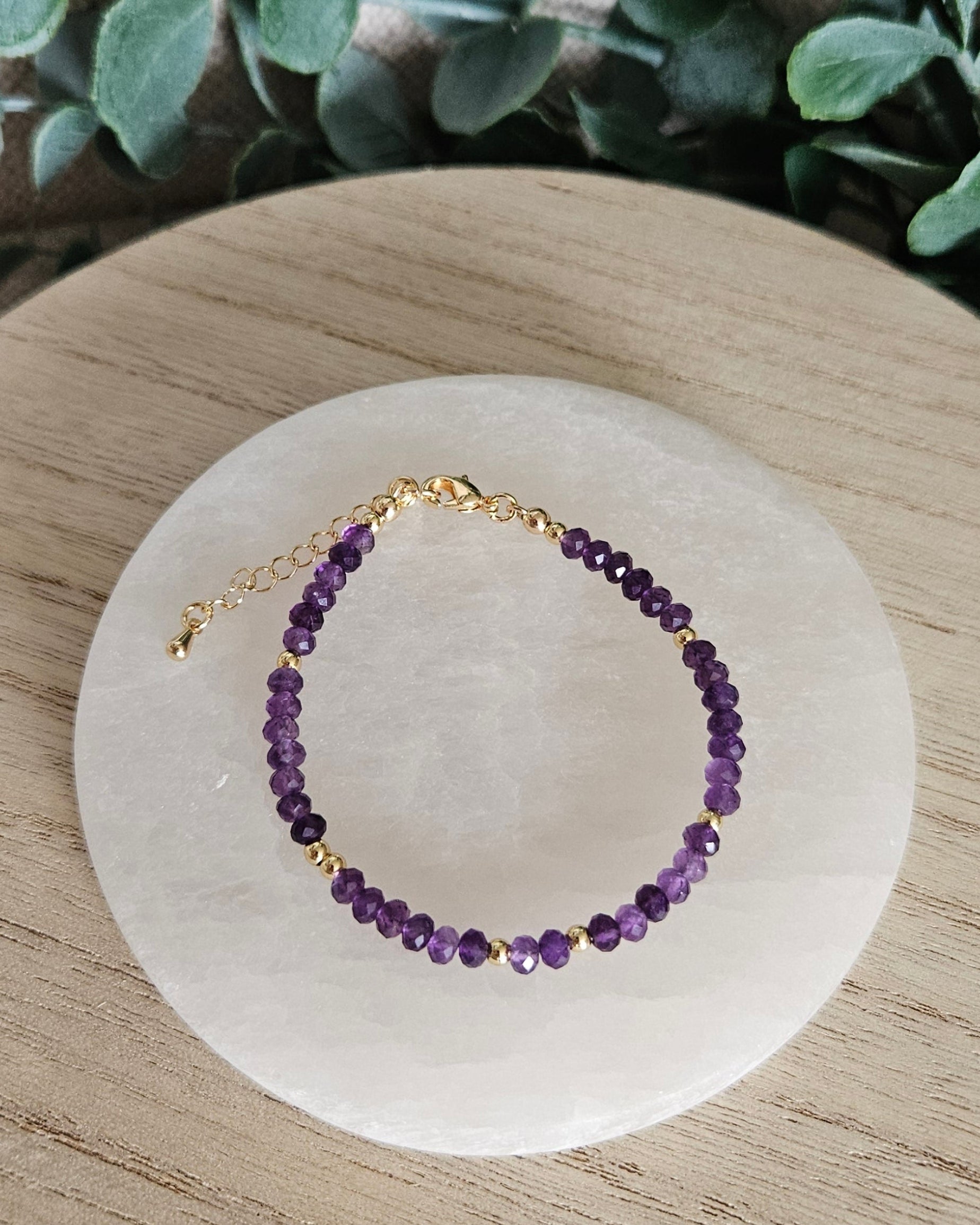 Overhead view of the adjustable Amethyst rondelle bracelet displayed on a round selenite plate