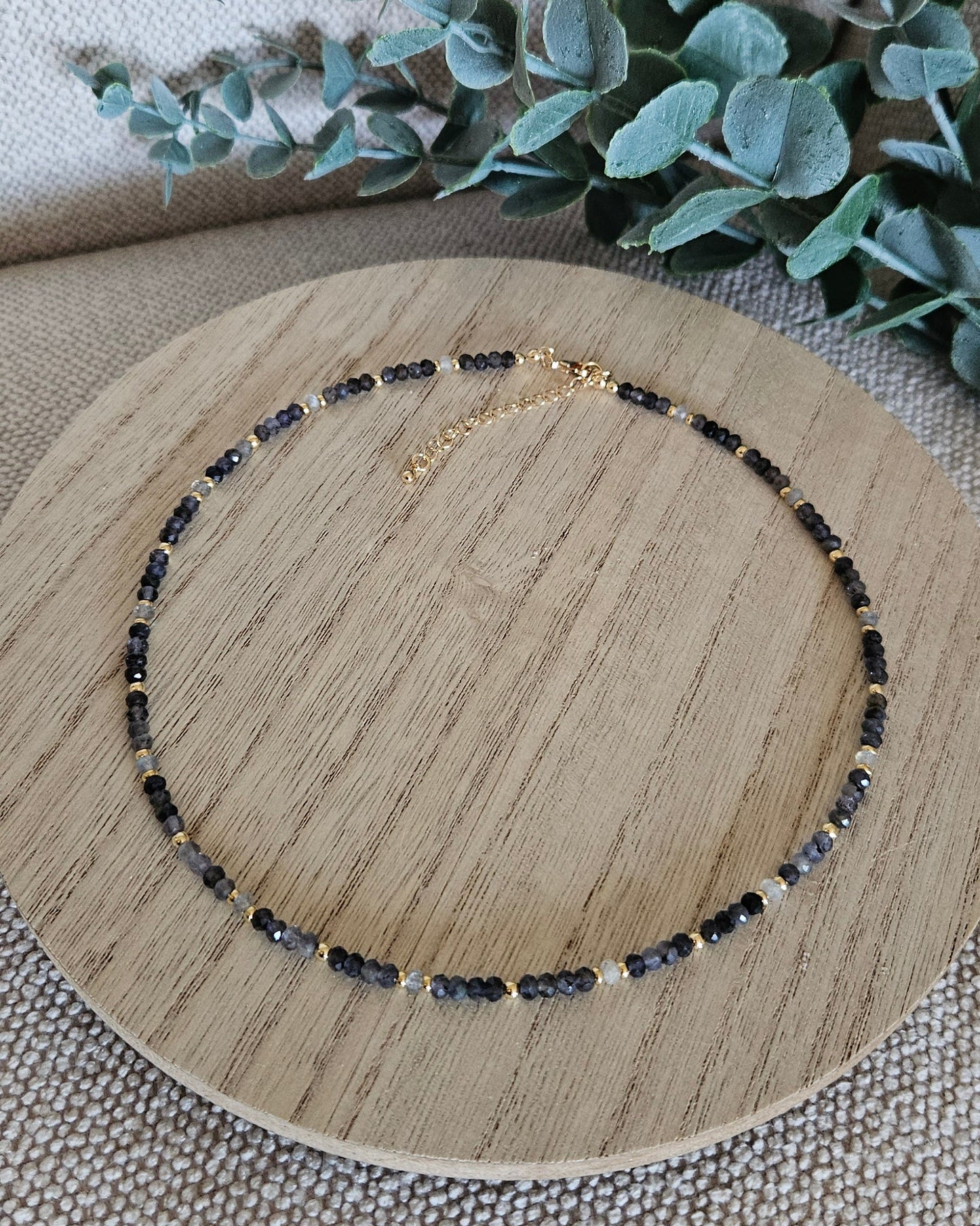 Overhead view of the complete Iolite and Labradorite necklace arranged on a round wooden display
