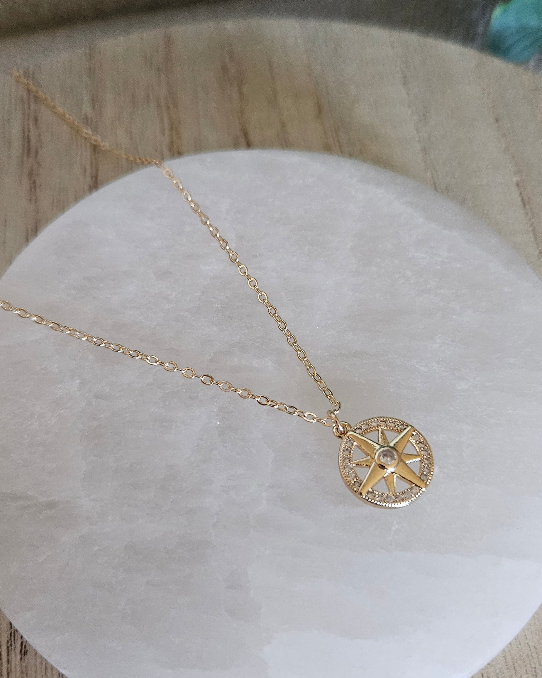 Overhead view of the gold-filled chain and North Star pendant arranged on a round selenite plate