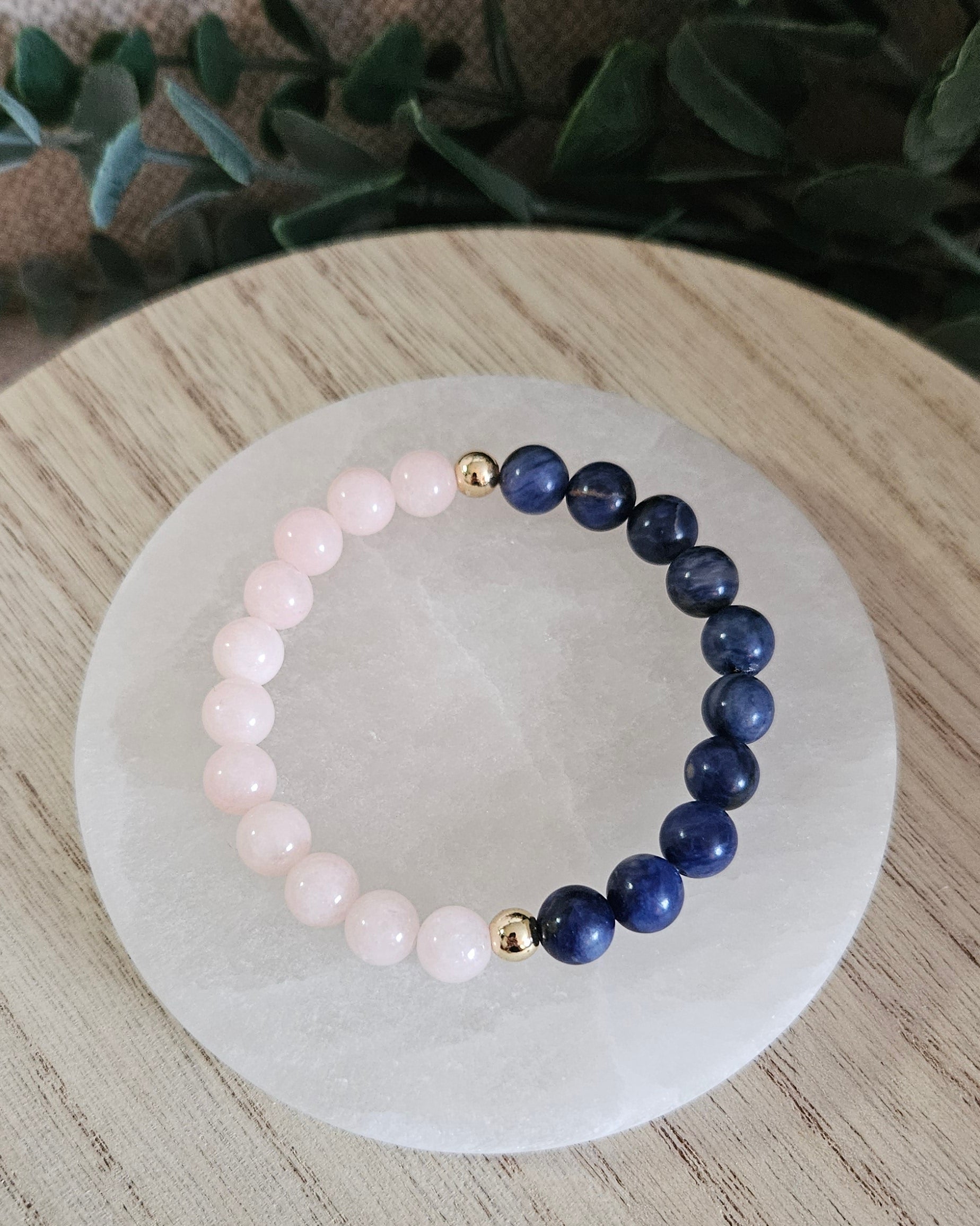 Overhead view of the pale Peach Jade and deep-blue Sodalite bracelet arranged on a round selenite plate