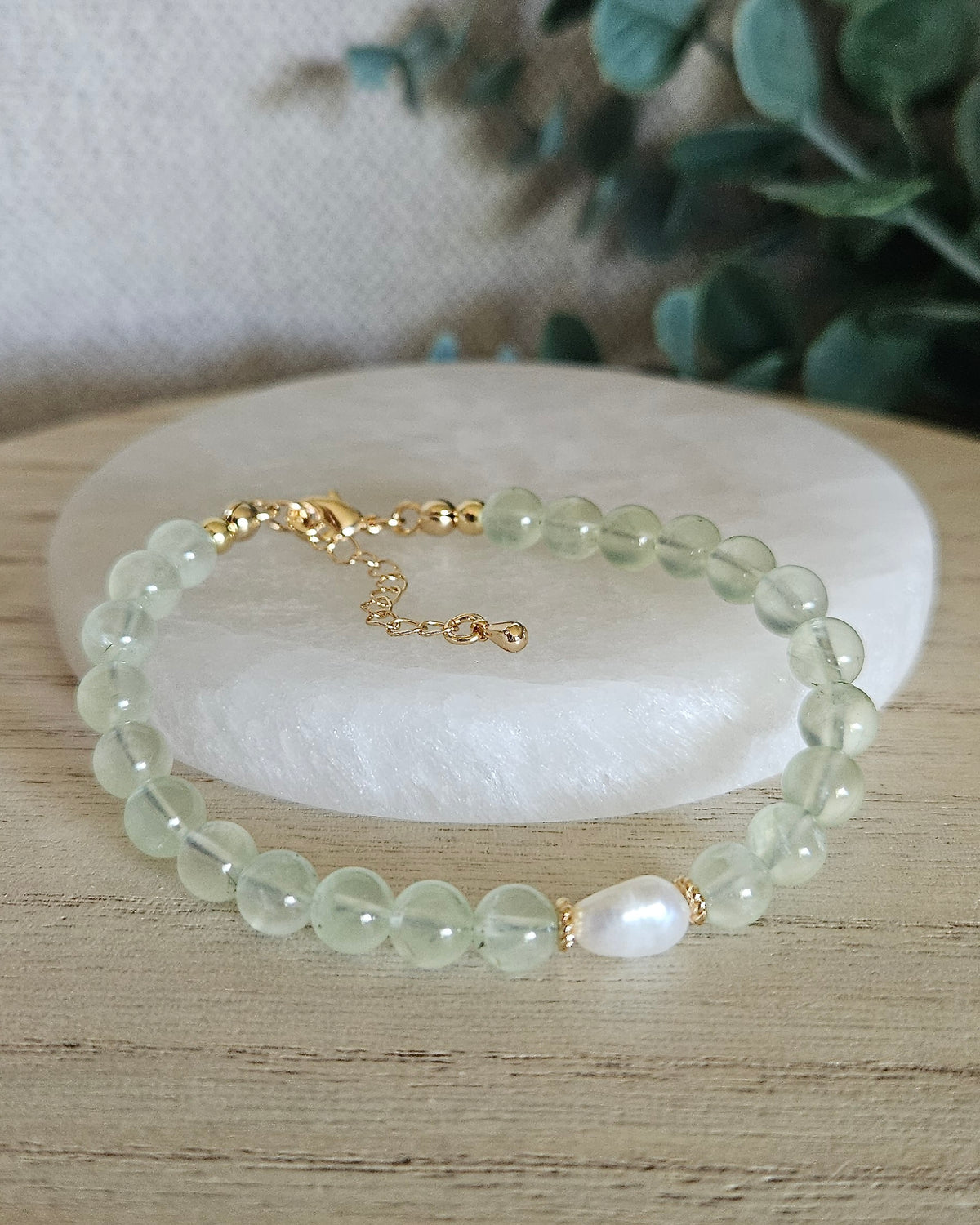 Prehnite and freshwater pearl bracelet with 14k gold-plated clasp and extender chain displayed on selenite with greenery in the background
