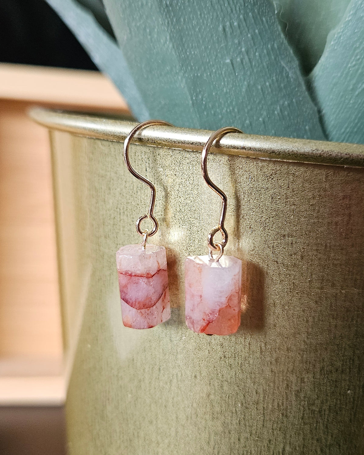 Red hematoid quartz earrings hanging from gold-plated stainless steel hooks against a warm neutral background