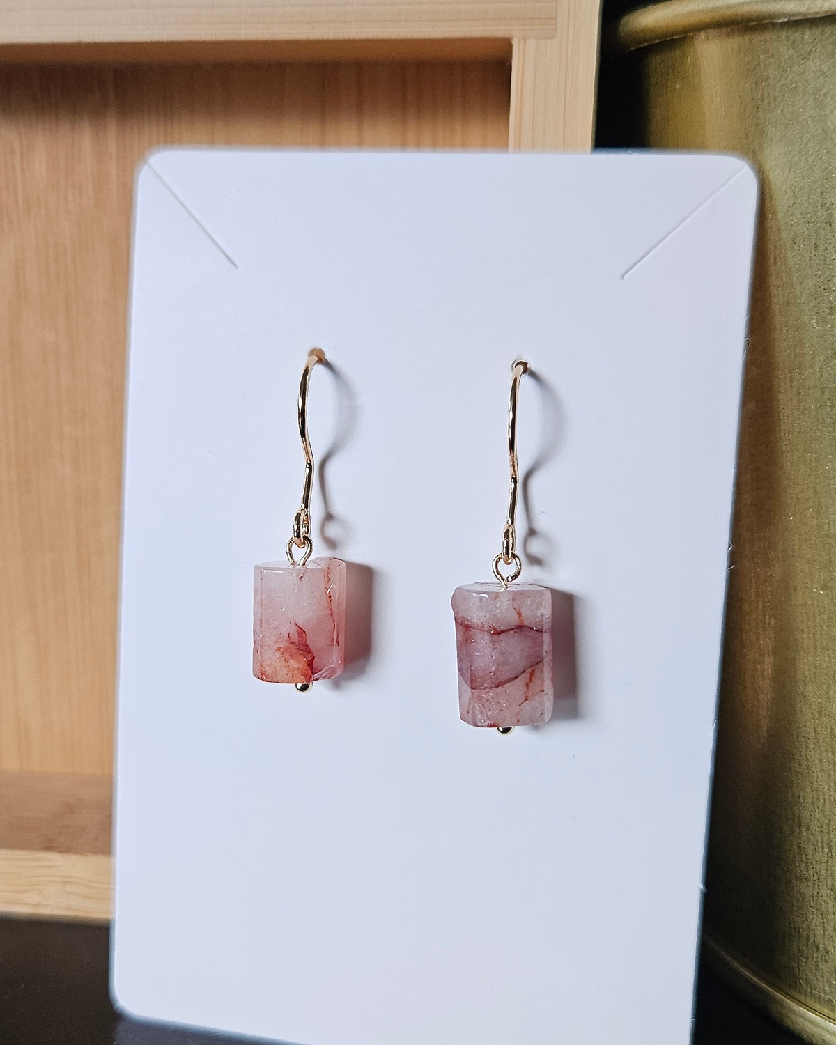 Red hematoid quartz gemstone earrings displayed on a white card with a natural wood background