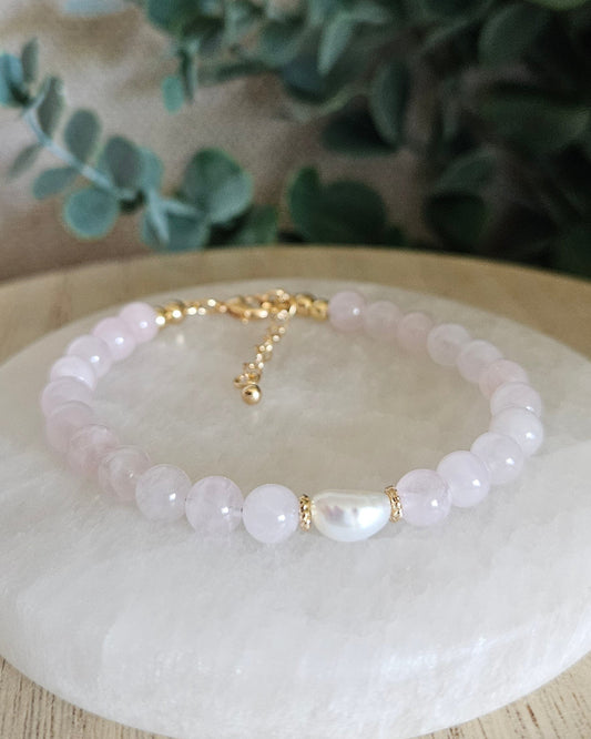 Rose Quartz Embrace bracelet with freshwater pearl focal and gold-plated accents displayed on a selenite plate