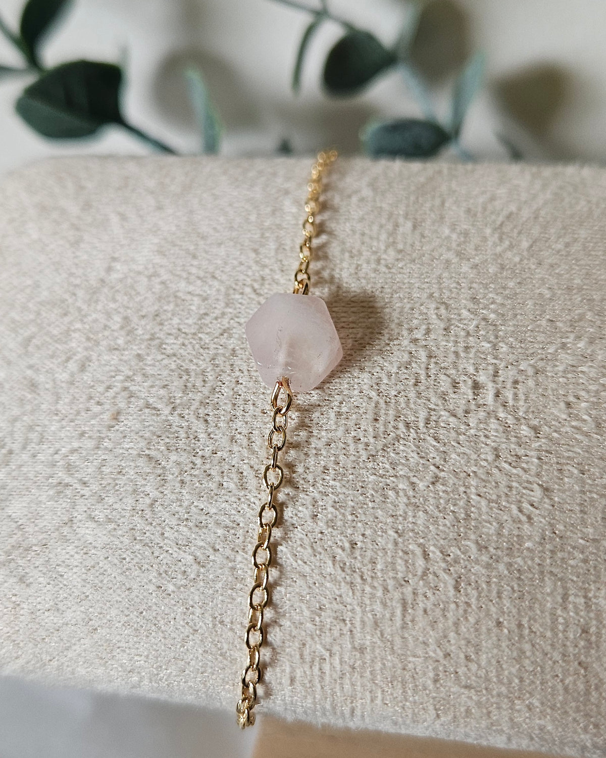Rose Quartz Whisper bracelet with a soft pink gemstone focal on a delicate 14k gold-plated chain displayed on a textured bracelet stand